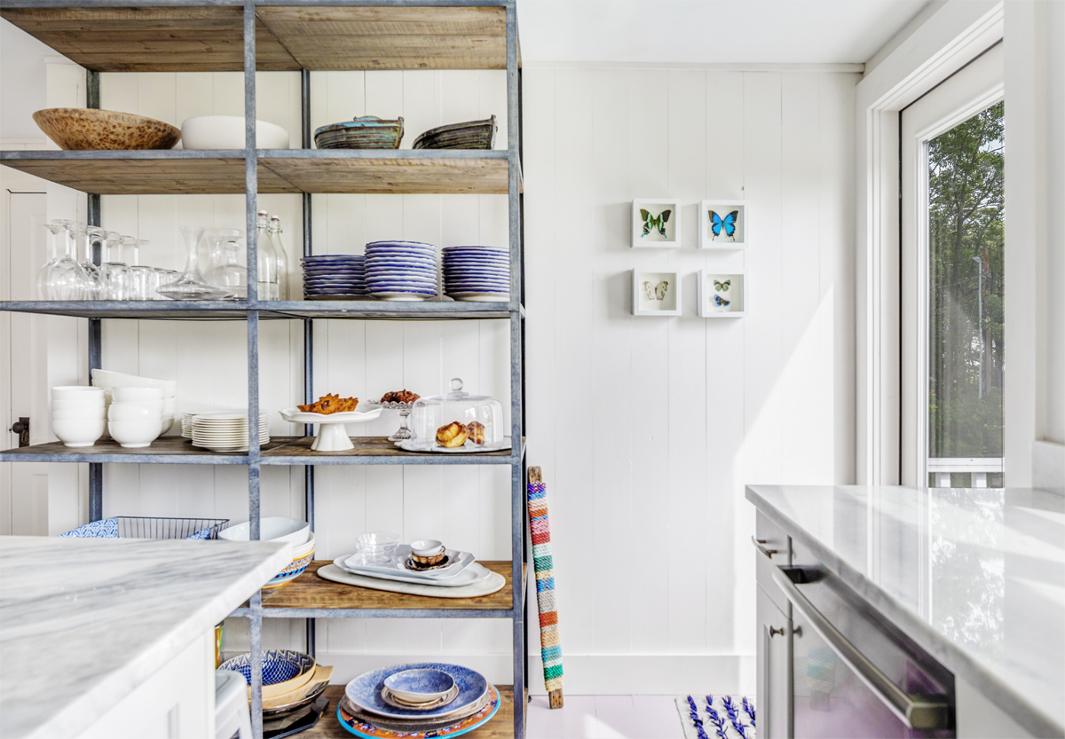 In the kitchen, counter stools tuck under a marble-topped island, and industrial-style open shelving holds tableware.