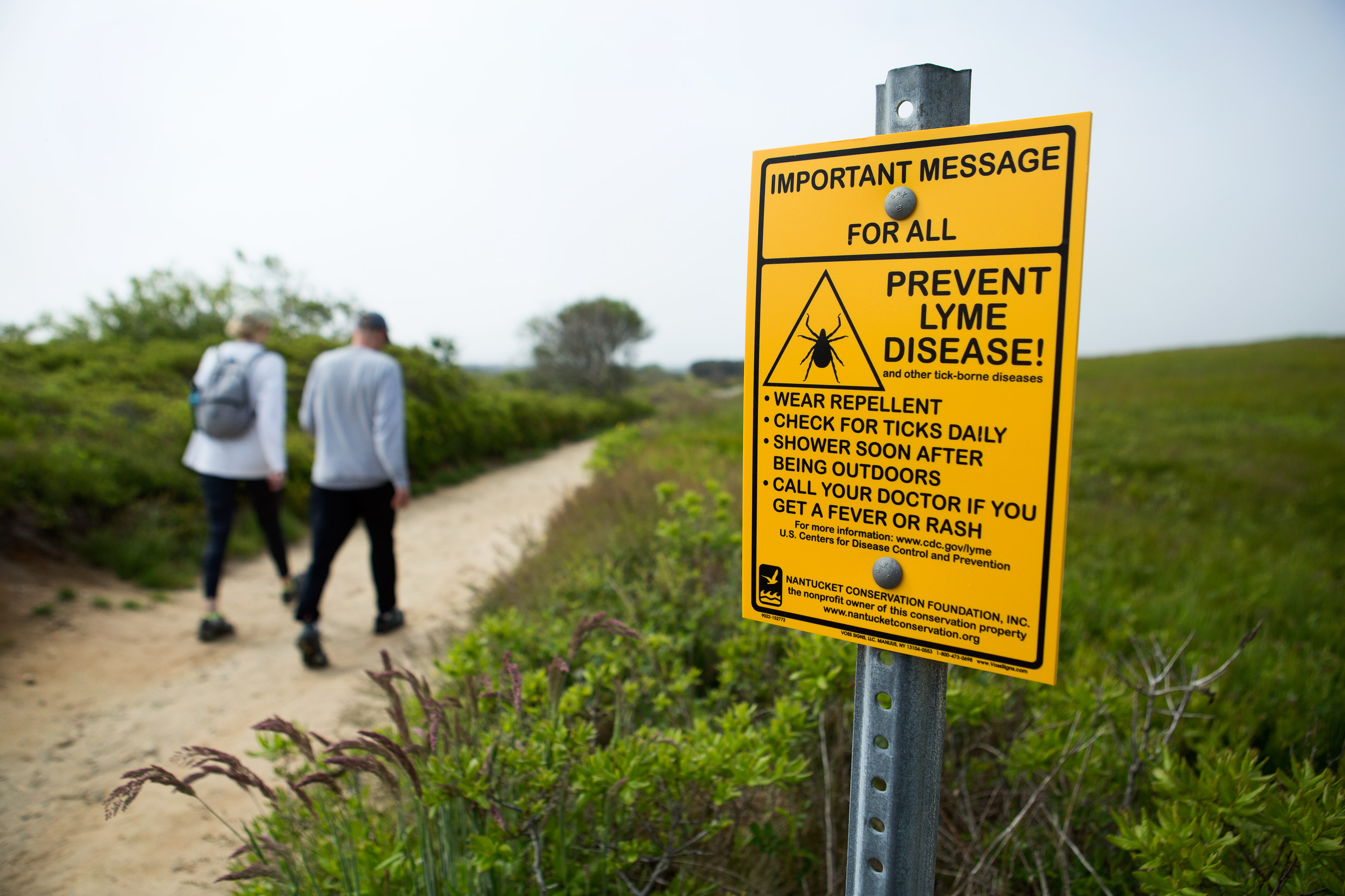 Hikers walked past a warning sign about ticks and Lyme Disease as they entered the "Sanford Farm, Ram Pasture, The Woods, Barn and Back Trail" hiking area in Nantucket, Massachusetts.