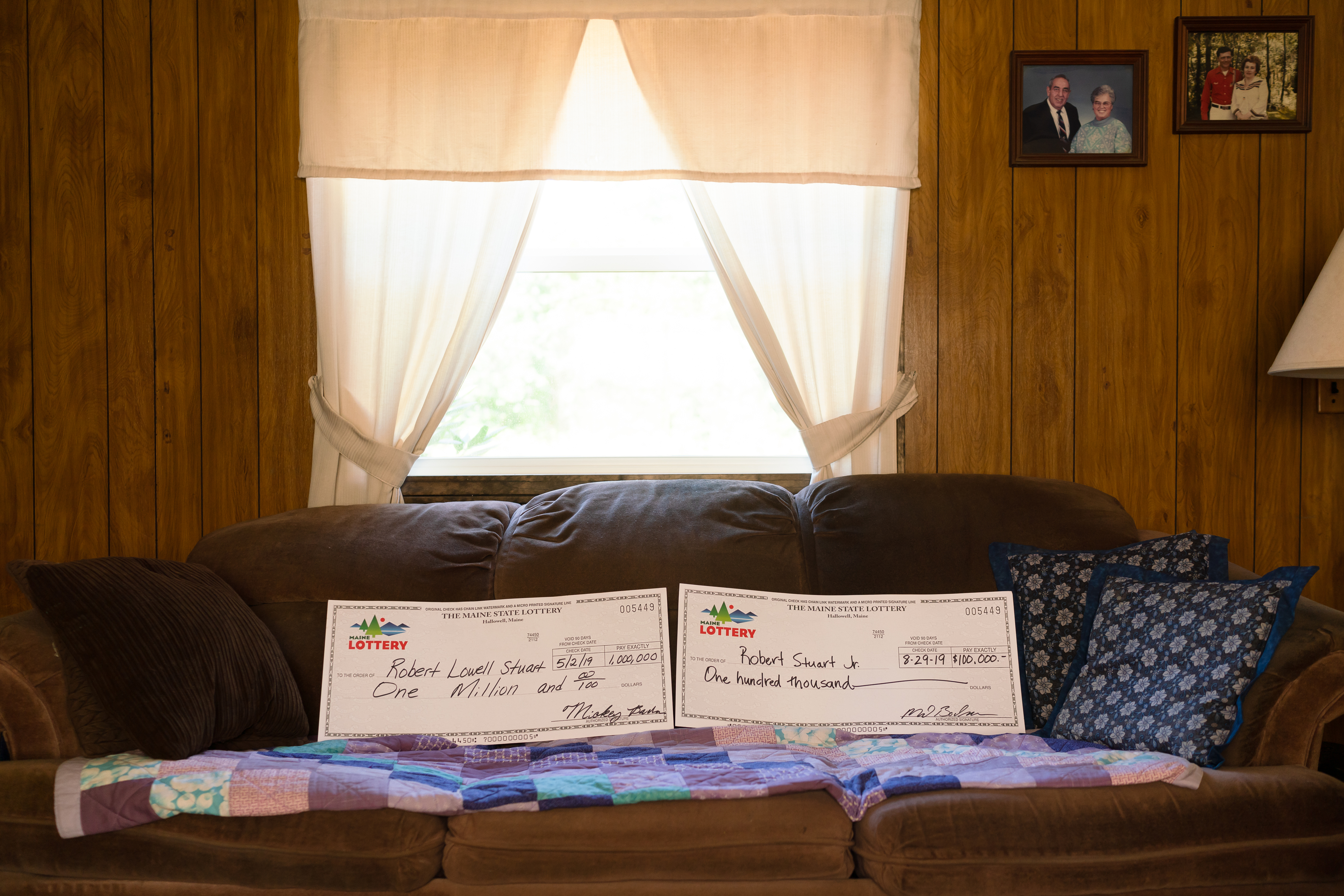 Two giant checks for Robert “Bobby” Stuart, which he received when he won the lottery twice, on his couch at his home in Kennebunkport, M.E.