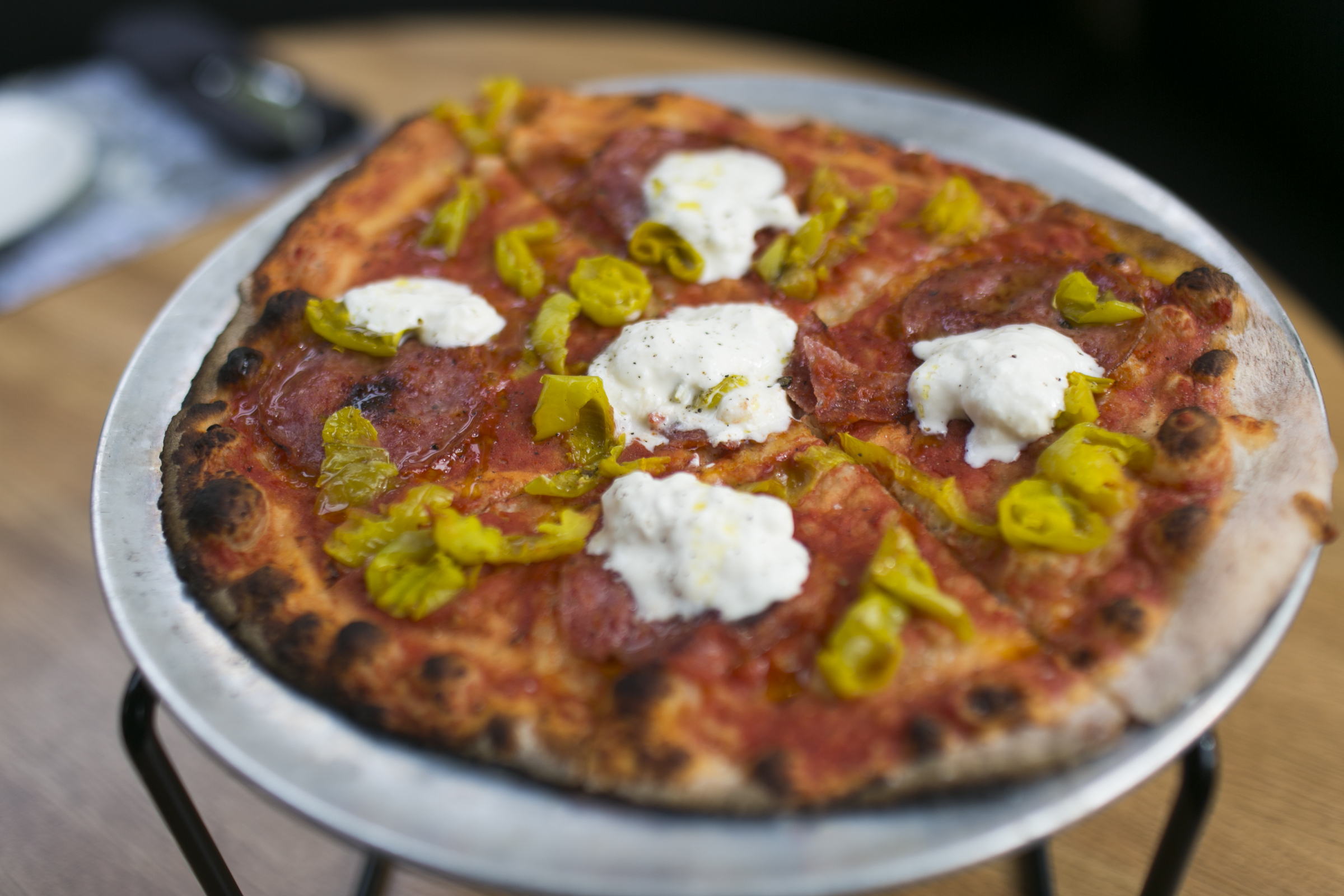 Pizza topped with sopressata, stracciatella, banana peppers, and red sauce.
