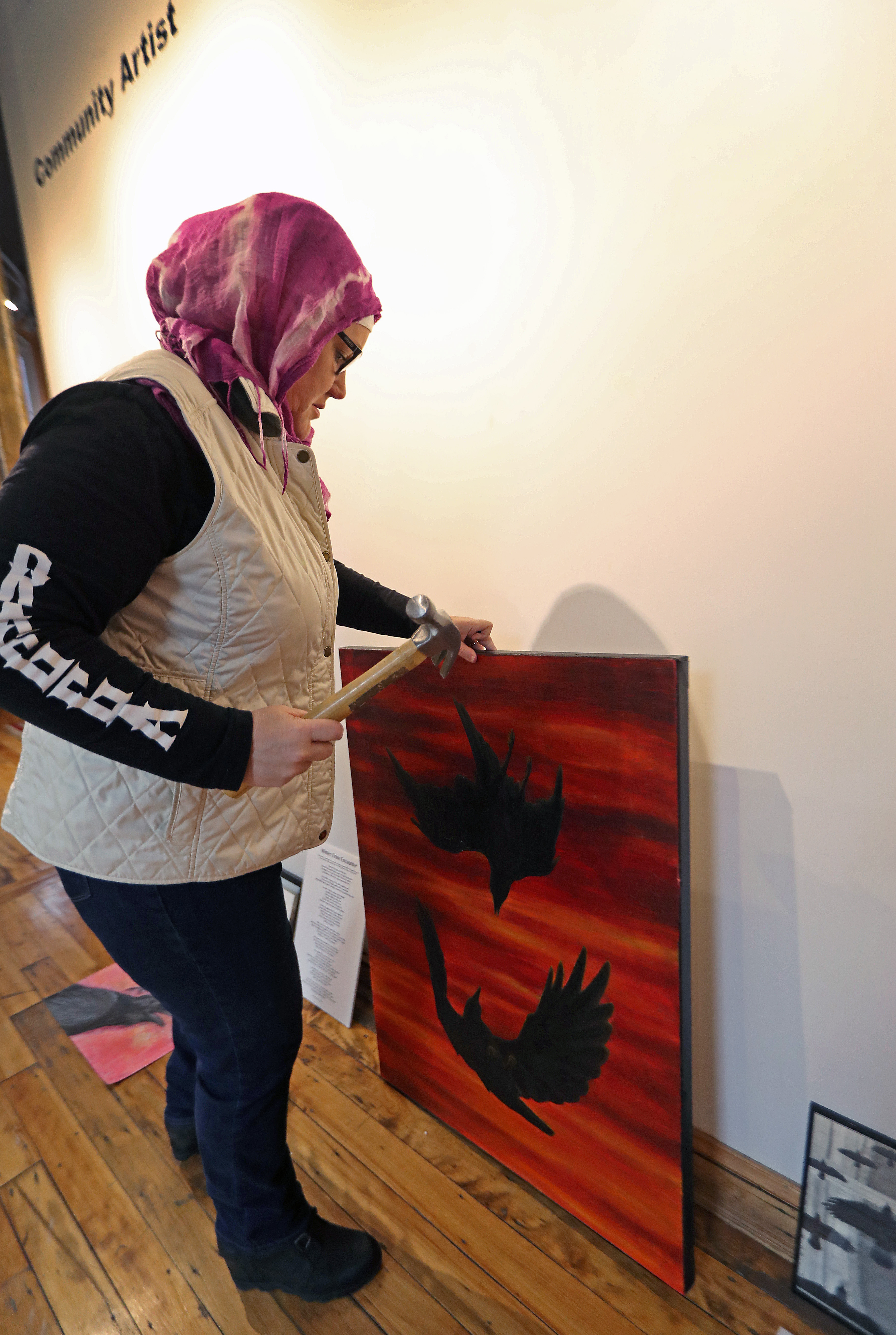 Anne Thiam, a board member of the Essex Art Center, worked on hanging a piece on the Community Artist wall at the Essex Art Center. The oil on canvas painting by Eric Allshouse is titled "Crow Fight."