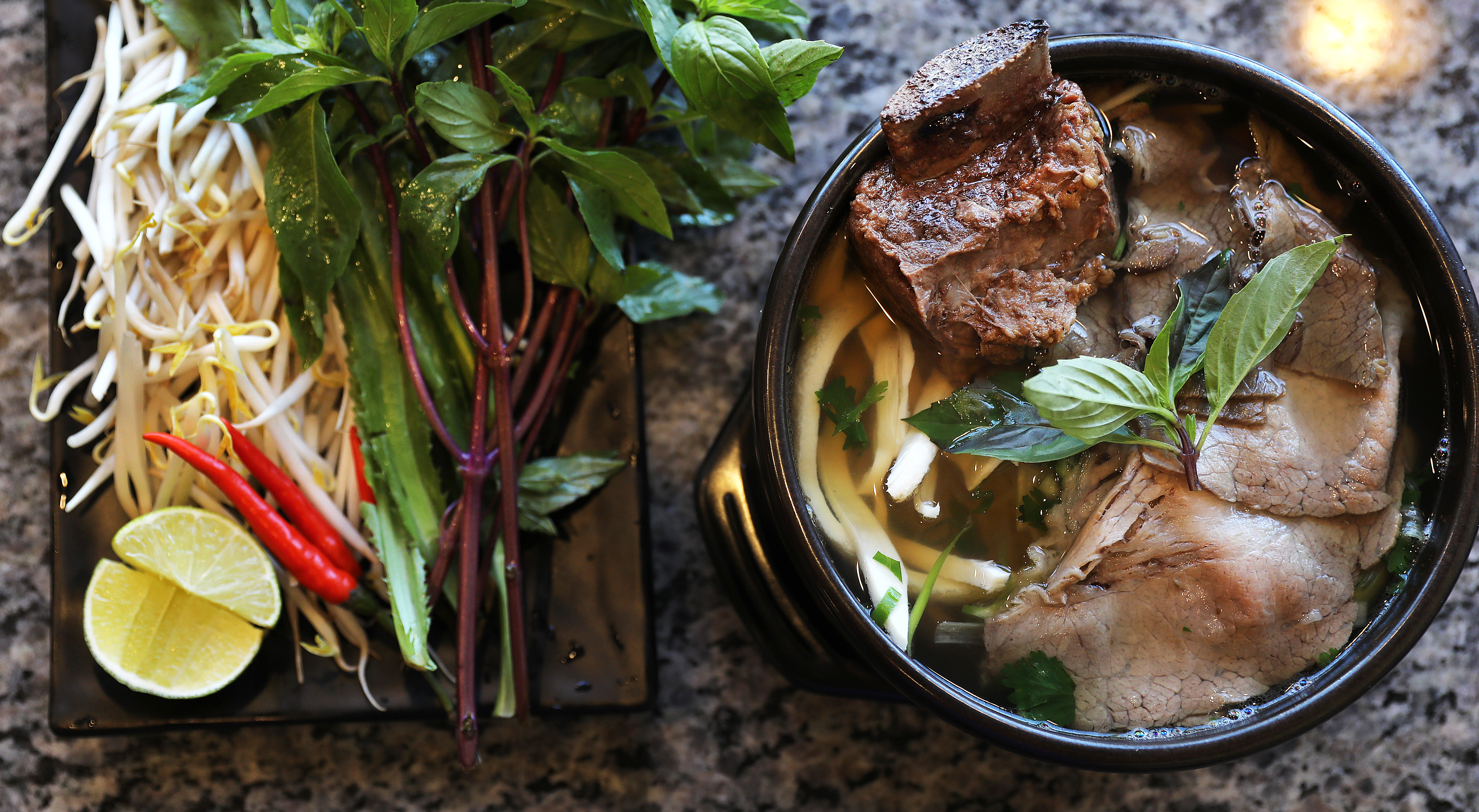 The Ban Tôi beef noodle soup is served with a side of bean sprouts, basil, chili peppers, and lime.