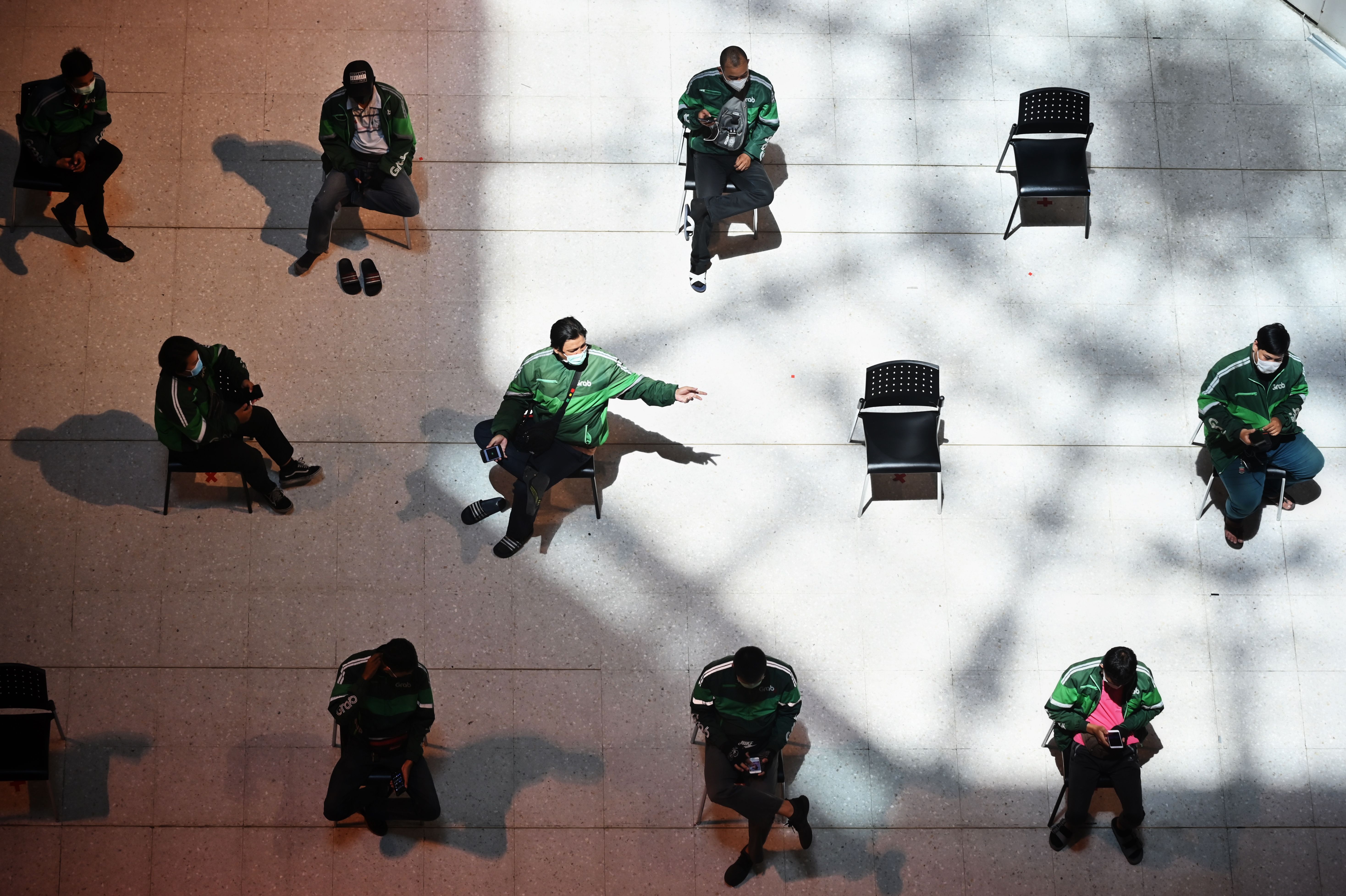 A group of Grab Food delivery drivers sat on chairs spaced apart for social distancing, as they wait for takeaway orders at Central Pinklao shopping mall in Bangkok.