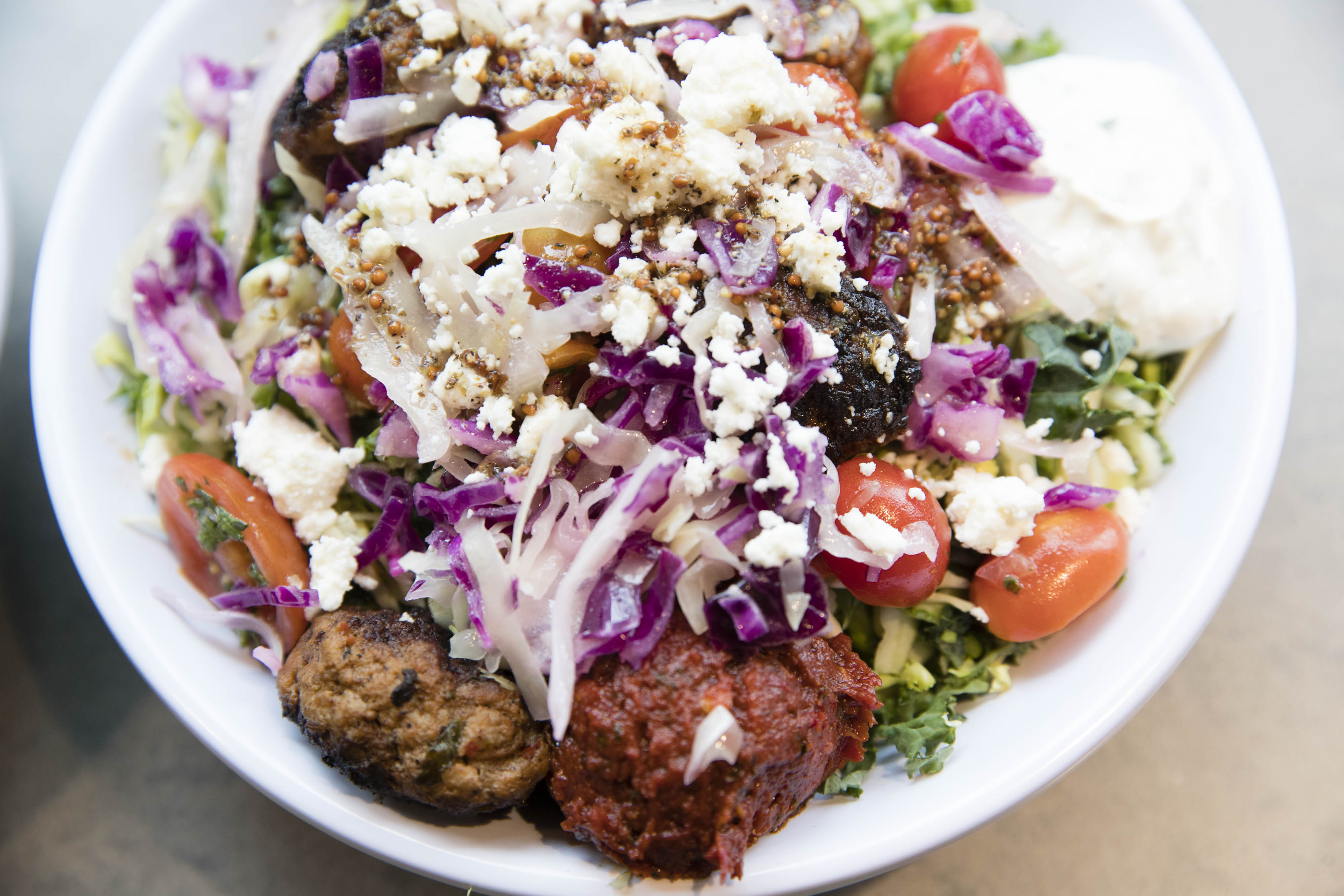 A super greens bowl with spicy lamb meatballs, hummus, tzatziki, harissa, tomato, onion, cabbage slaw, crumbled feta, and greek vinaigrette at Cava on Boylston Street.