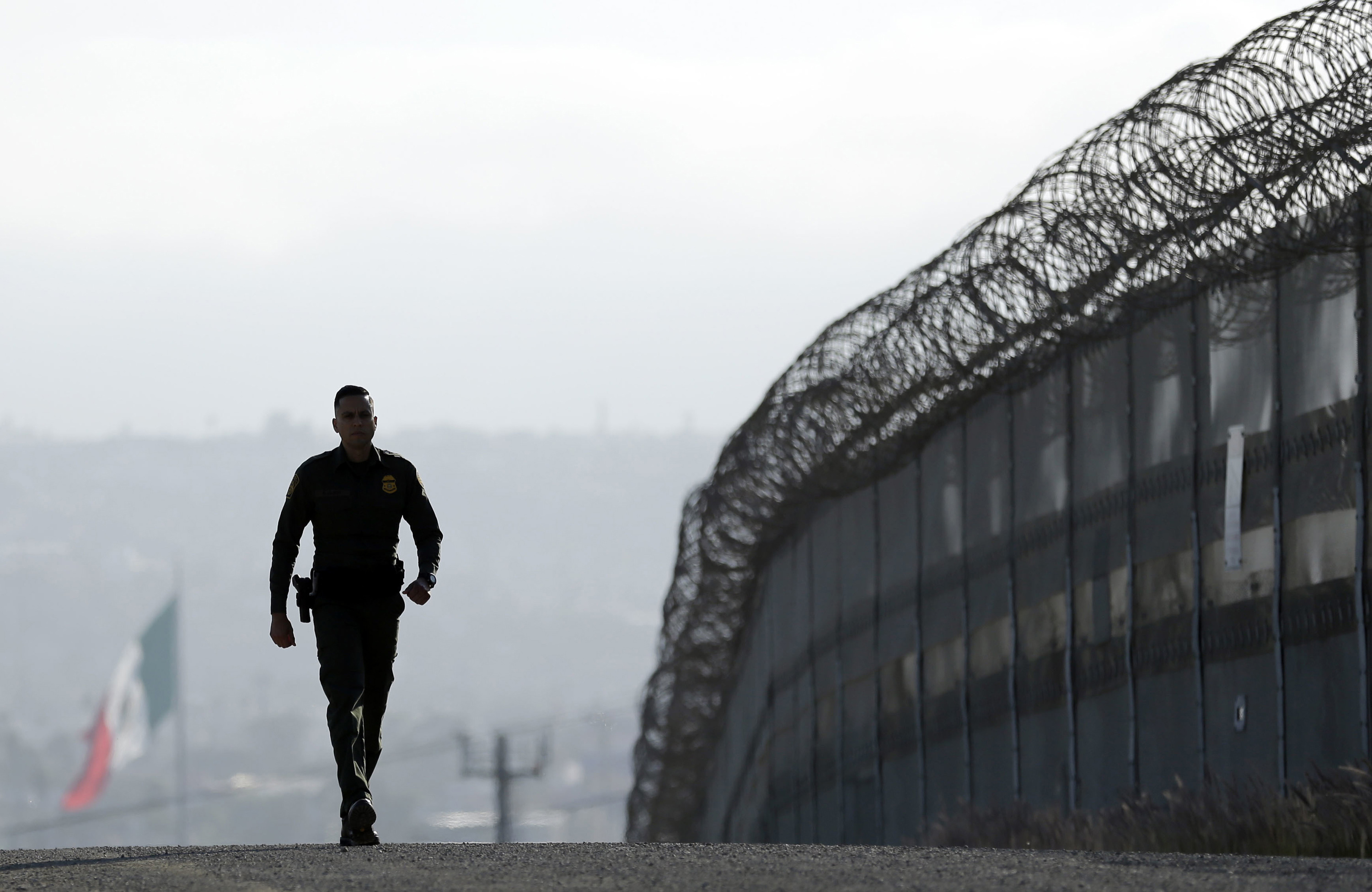 Border Patrol agent Eduardo Olmos walked near the secondary fence separating Tijuana, Mexico, background, and San Diego in San Diego.