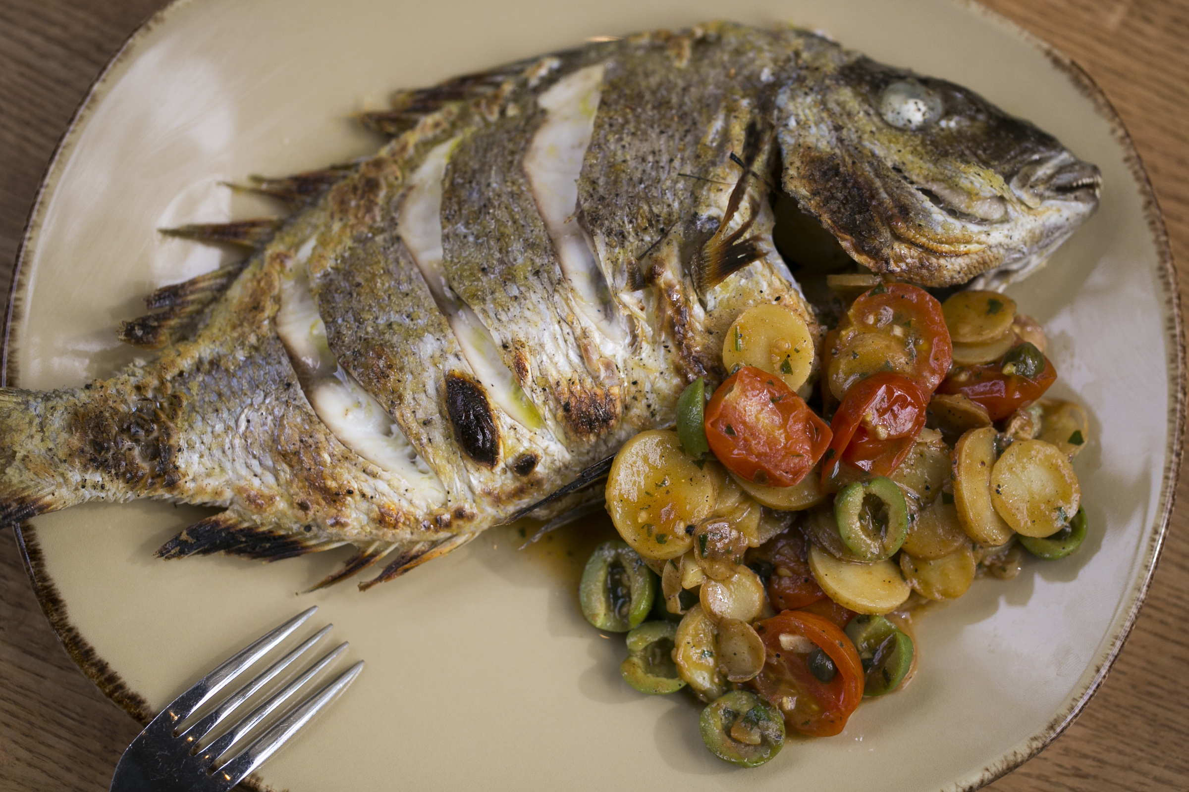 Whole roast fish with potatoes, tomatoes, and olives.