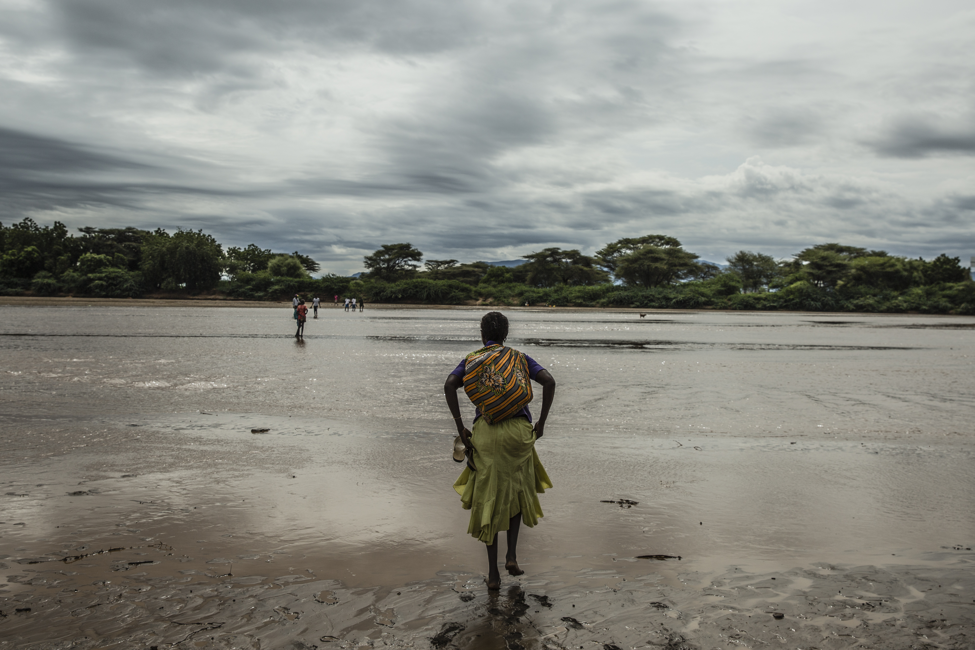 A woman hitches up her skirt to cross the Tarach River at the UNHCR refugee camp .