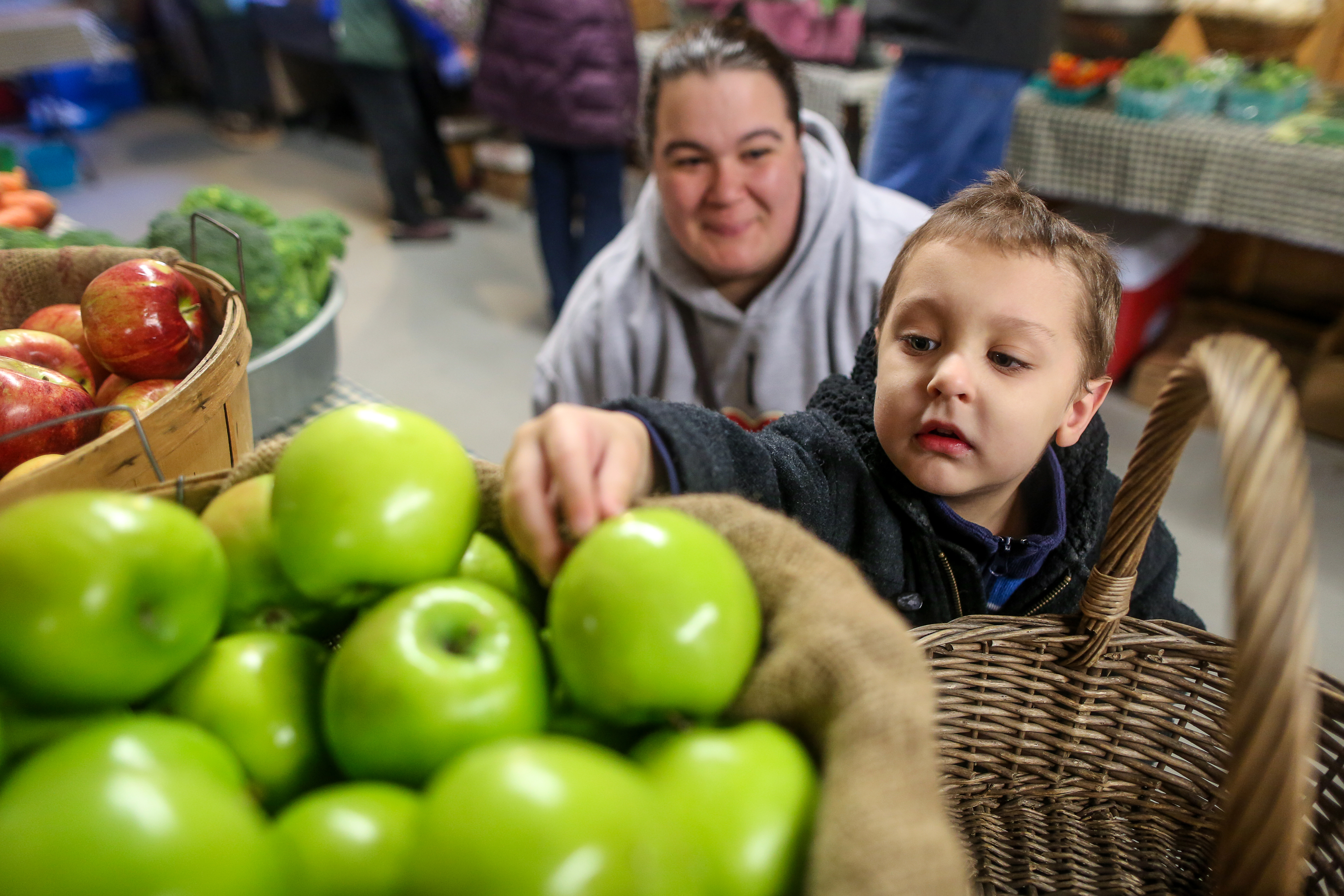 Kathy Trainor (left) of Taunton, watches her son John Trainor 4, choose an apple from the Oakdale Farms stand at the Easton Winter Farmers Market at Simpson Spring in Easton.