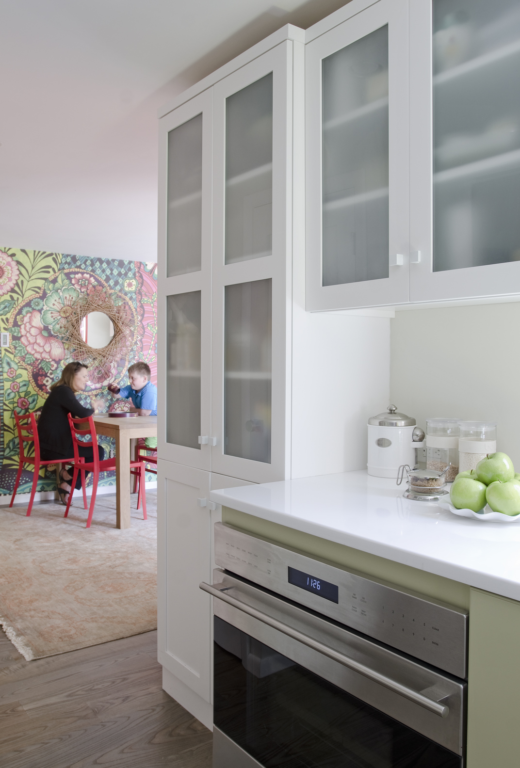 A floor-to-ceiling pantry with frosted glass houses not just food but also the toaster and microwave. A full-size Wolf oven sits under a white Silestone countertop.