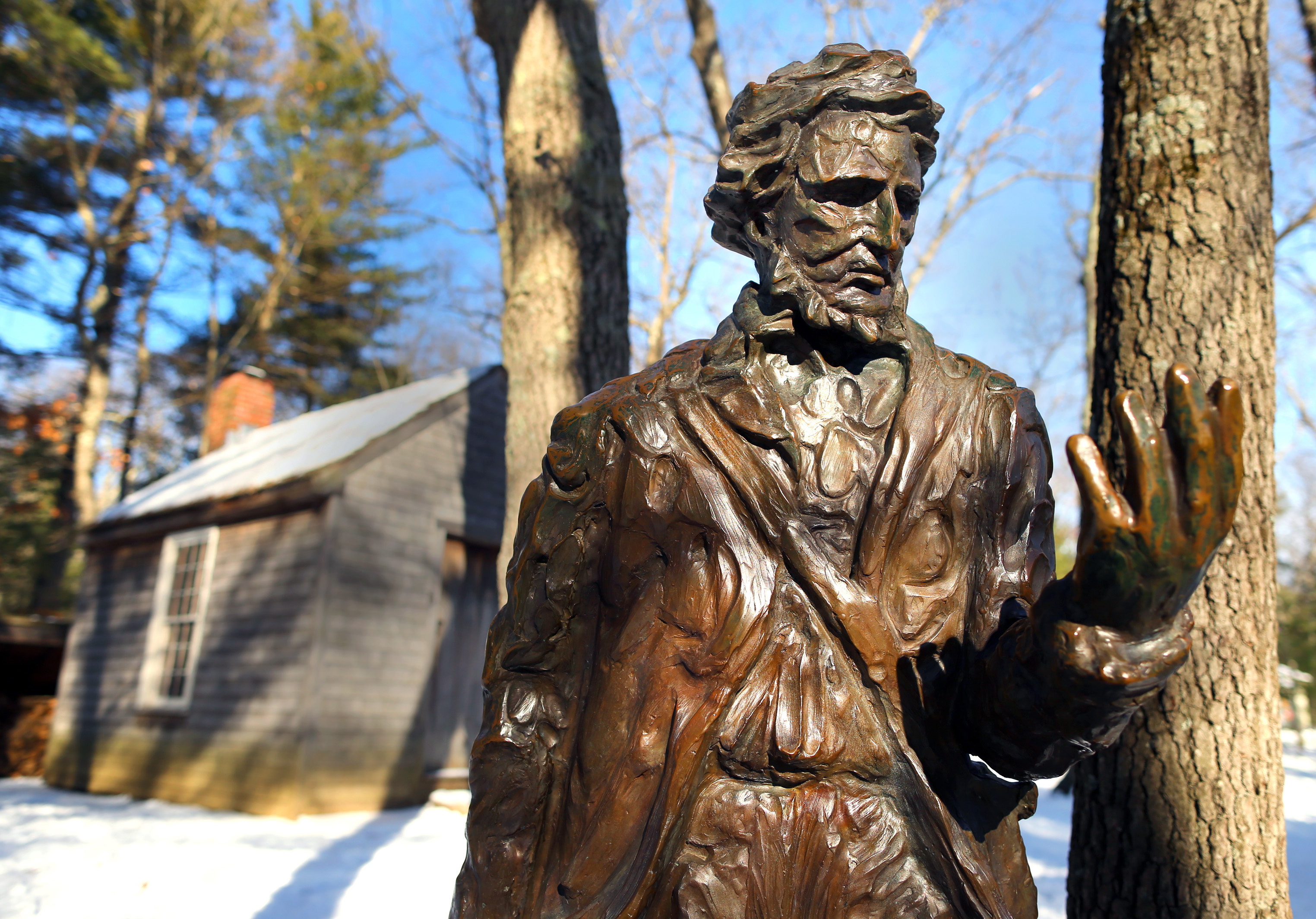 A statue of Henry David Thoreau in front of a reproduction of his cabin at the Walden Pond Reservation.