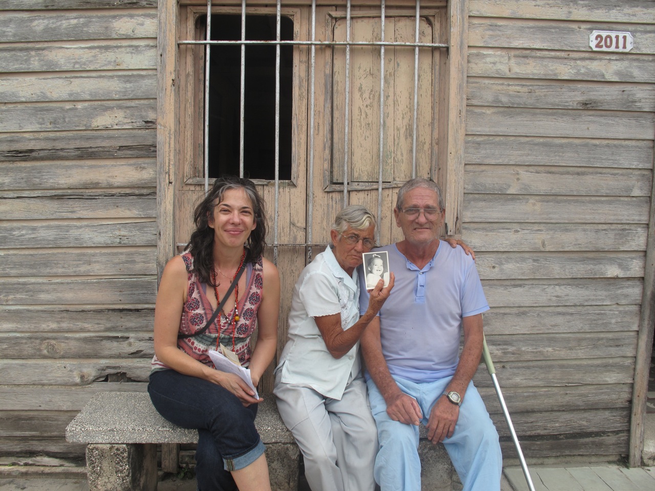 Lopez (left) during a 2011 visit to the town where her parents lived in Cuba. With her are Juanita Miranda — holding a photo of Lopez as a baby — and her husband, Alfonso, in front of their home.