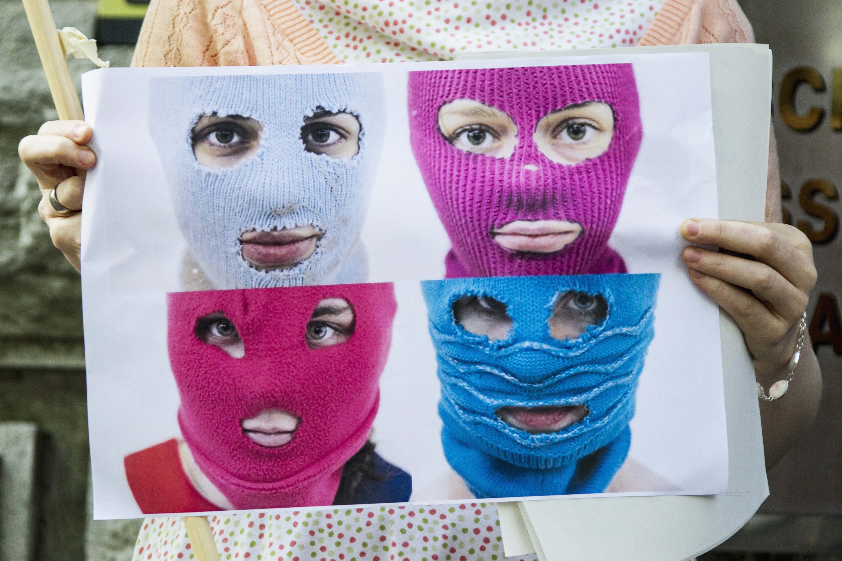 A protester holds a placard of pictures of people wearing balaclavas, in the style of the arrested performers, outside the Russian embassy in Berlin.