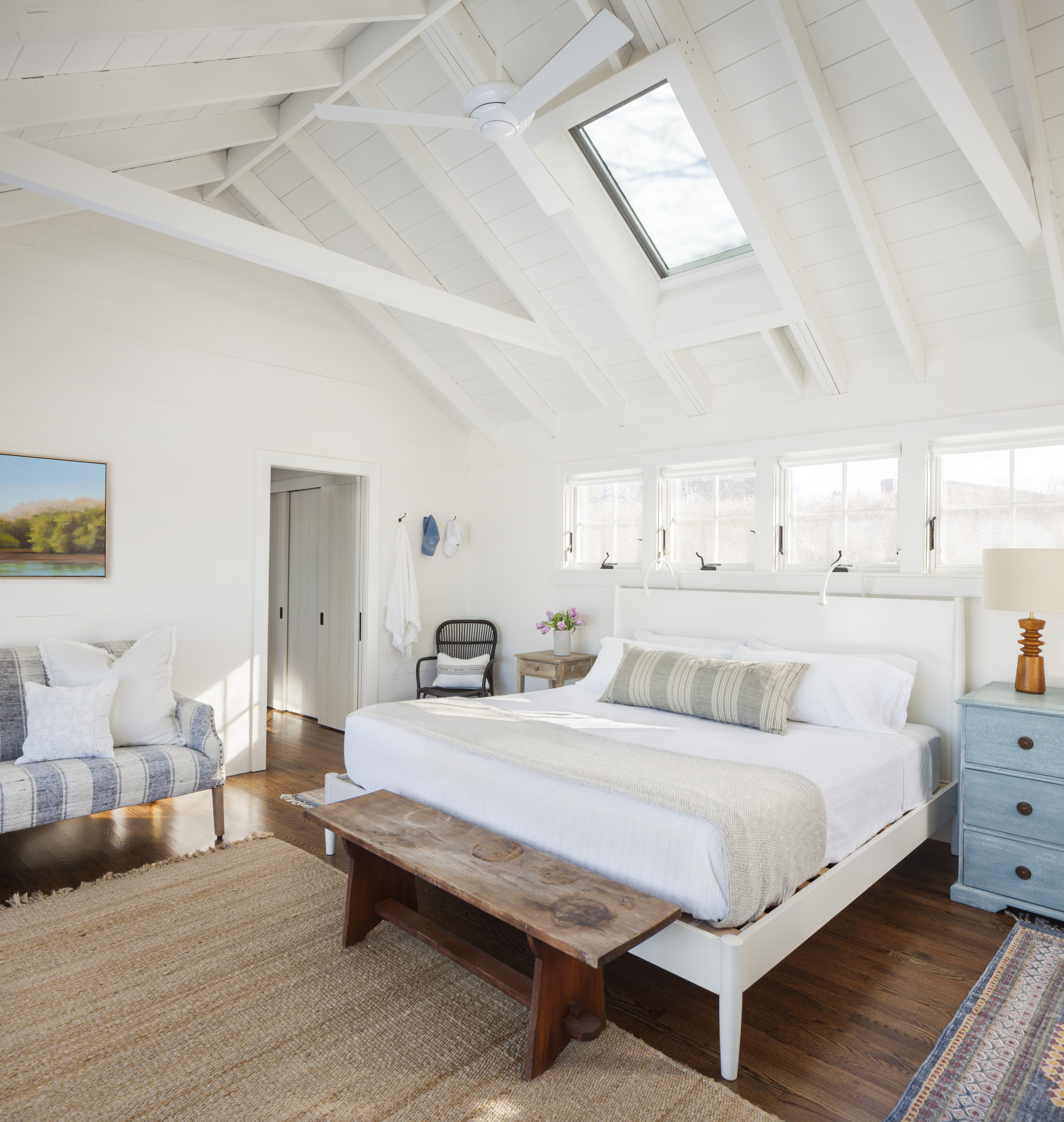 In the master bedroom, the colors of the striped settee from Terrain and washed-blue Dubois dresser from Wisteria – used as a night stand – echo the ocean view opposite the bed. The patterned throw rugs beside the bed are from Mohr & McPherson in Boston.