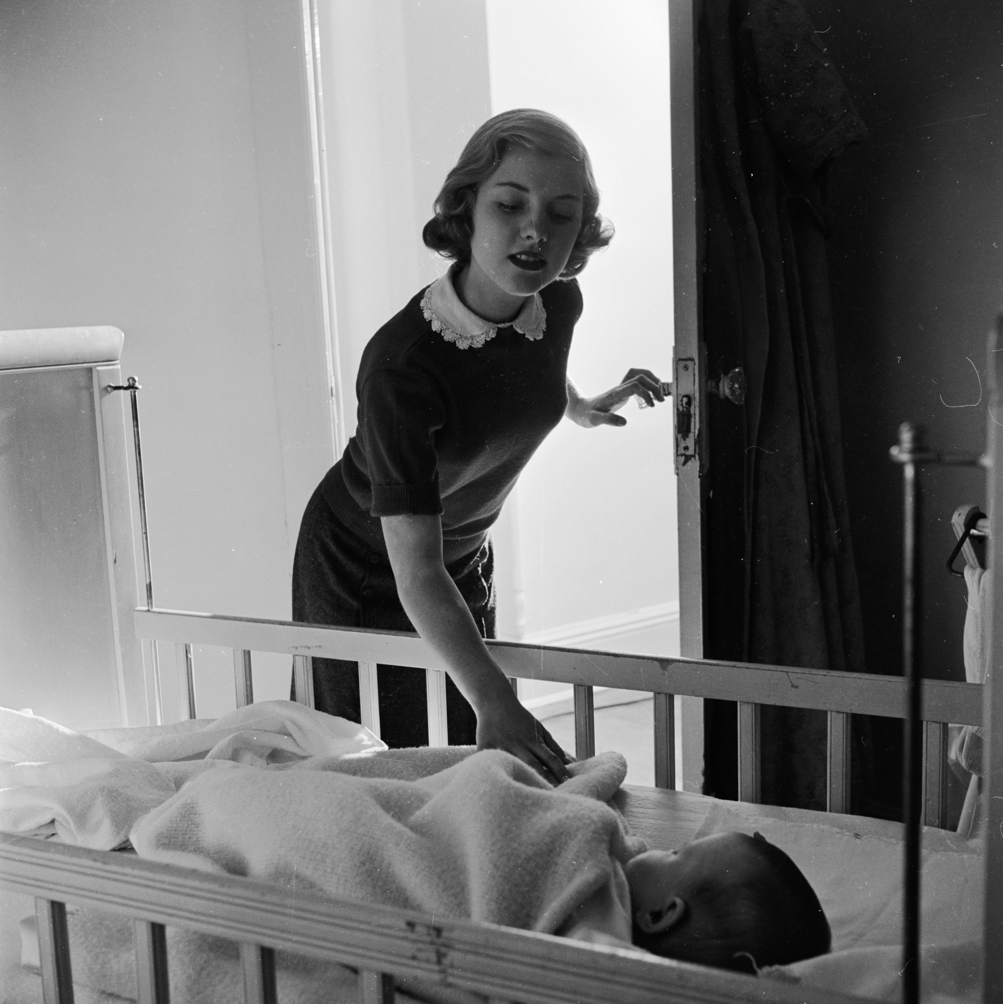 Circa 1948: A baby-sitter keeps a watchful eye on a sleeping child.