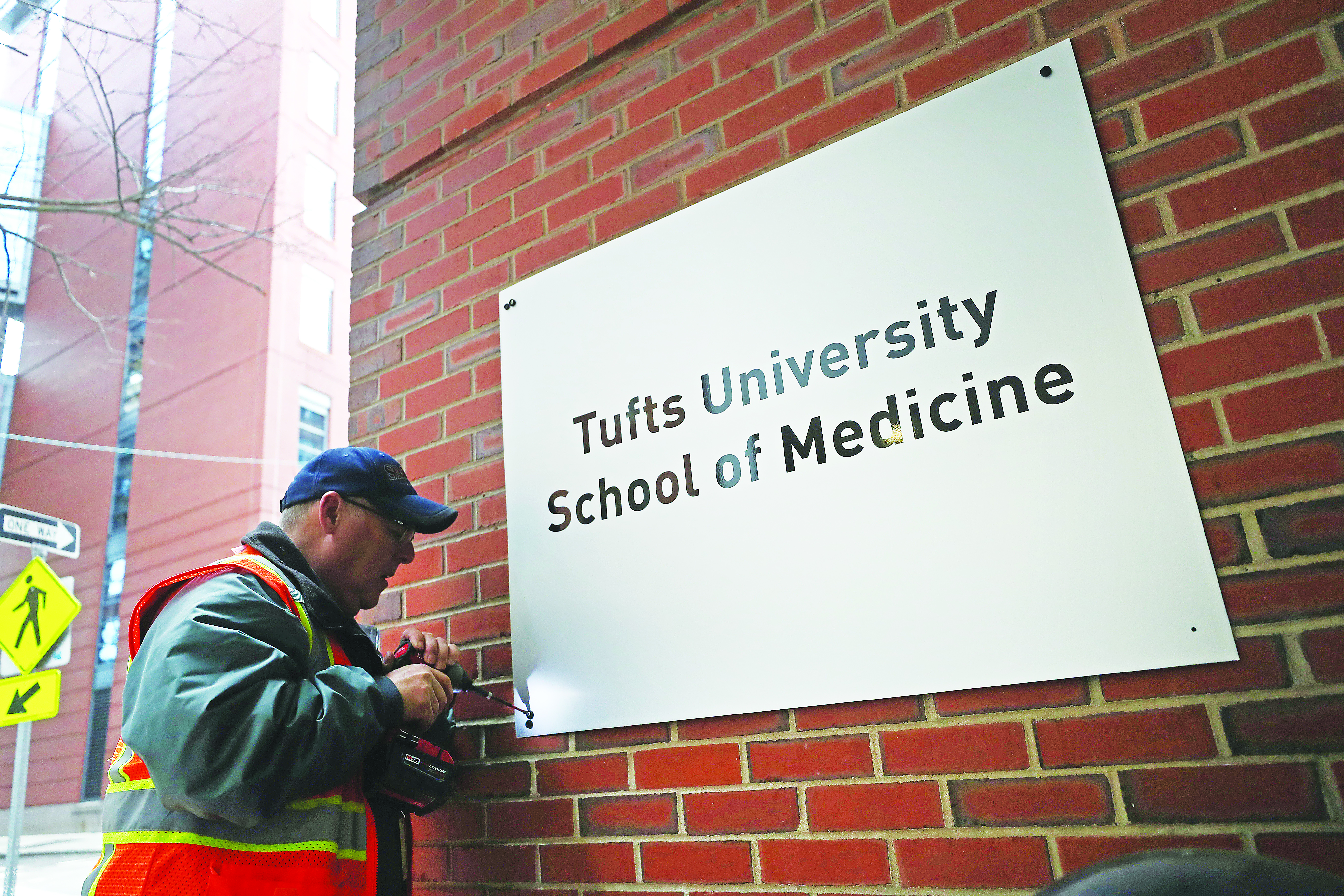 Scott Suleski with Sign Design & Sales covered over a sign bearing the Sackler family name on the Tufts building at 145 Harrison Ave. in Boston.