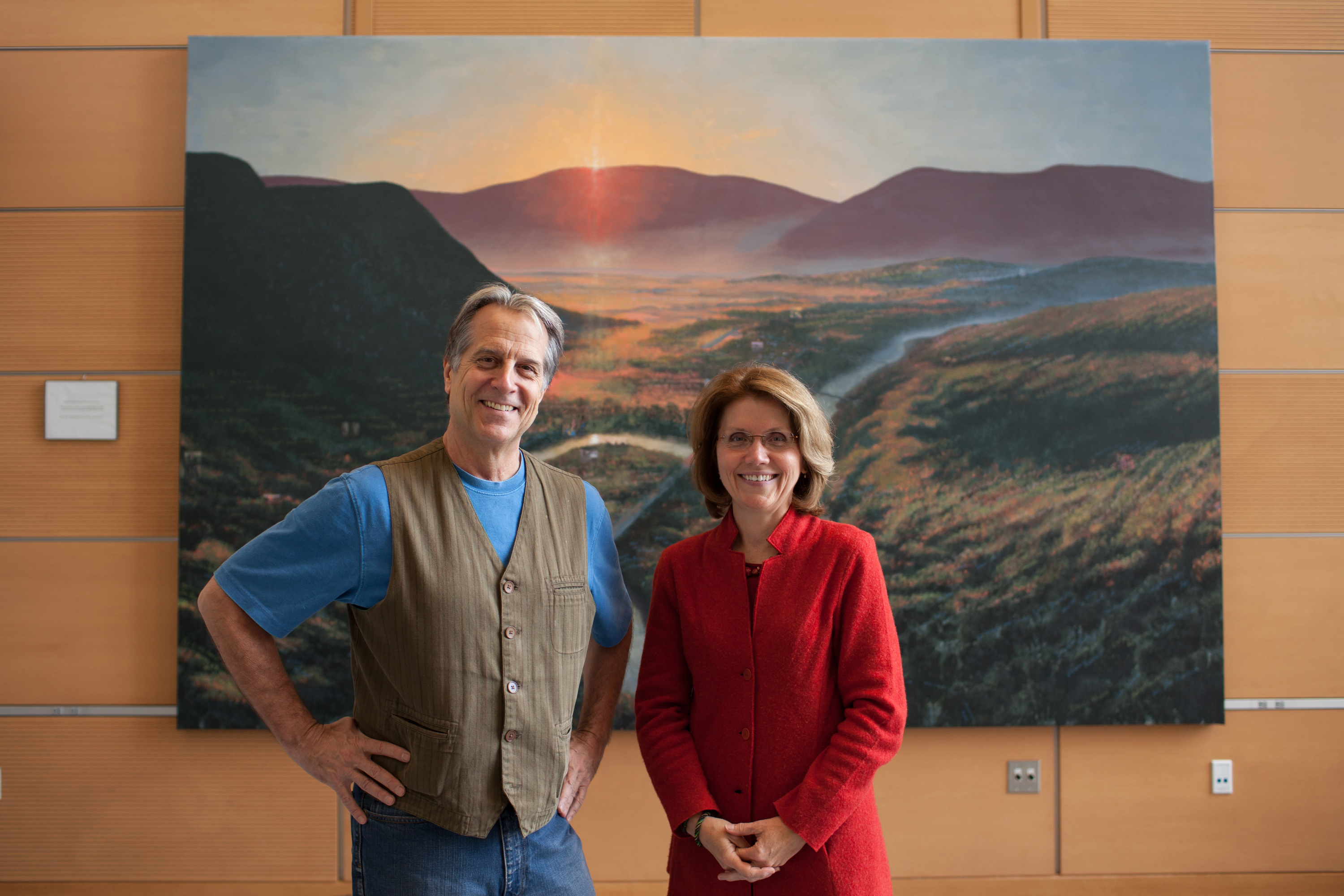 Two figures in North Adams’ revival, artist Steve Hannock and Massachusetts College of Liberal Arts president Mary Grant, with his painting in the school’s new science center.