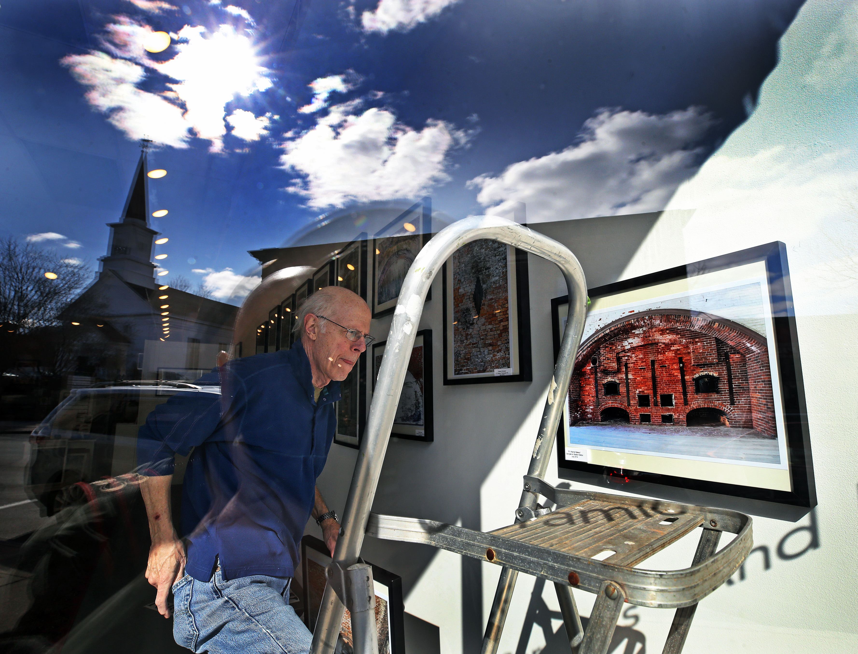 Roy DiTosti was photographed through a window on Main Street in Maynard as he was hanging his, photography exhibit "Obsolete Military Structures" at 6 Bridges Gallery.