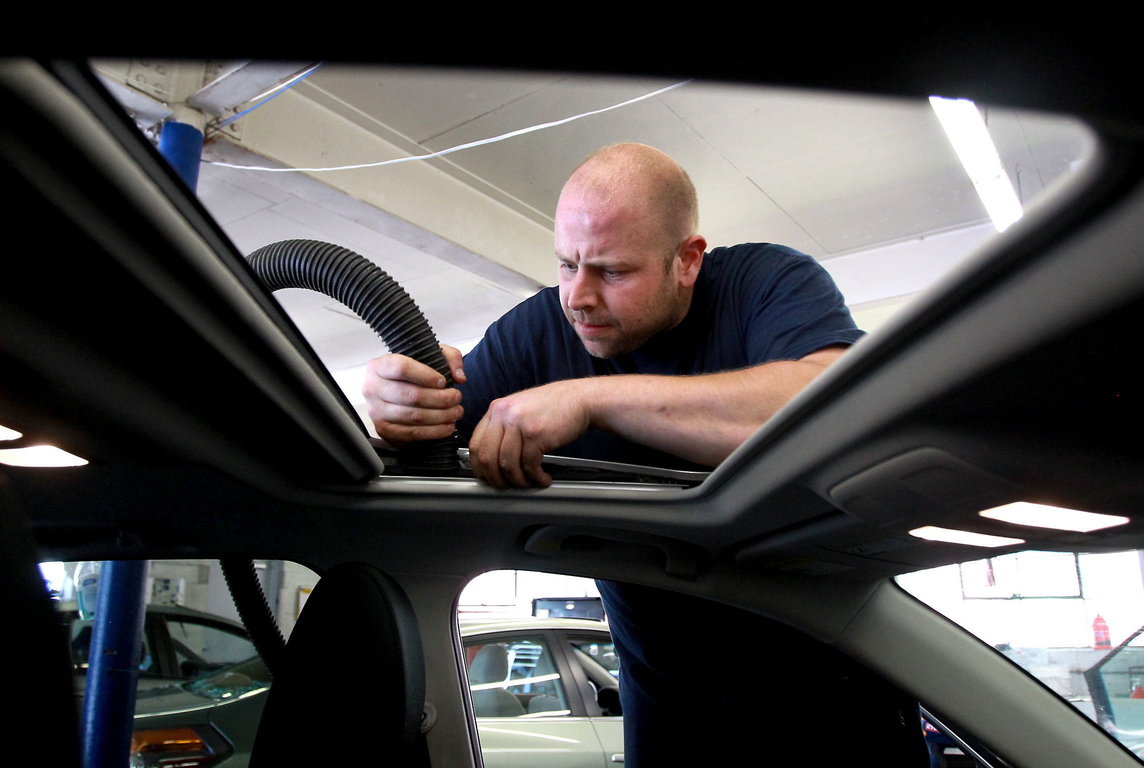Derek Baldassarre vacuumed broken glass from the sunroof of a car at JN Phillips Auto Glass in Newton. Auto body shops have been swamped since the storm pummeled the area on Tuesday.