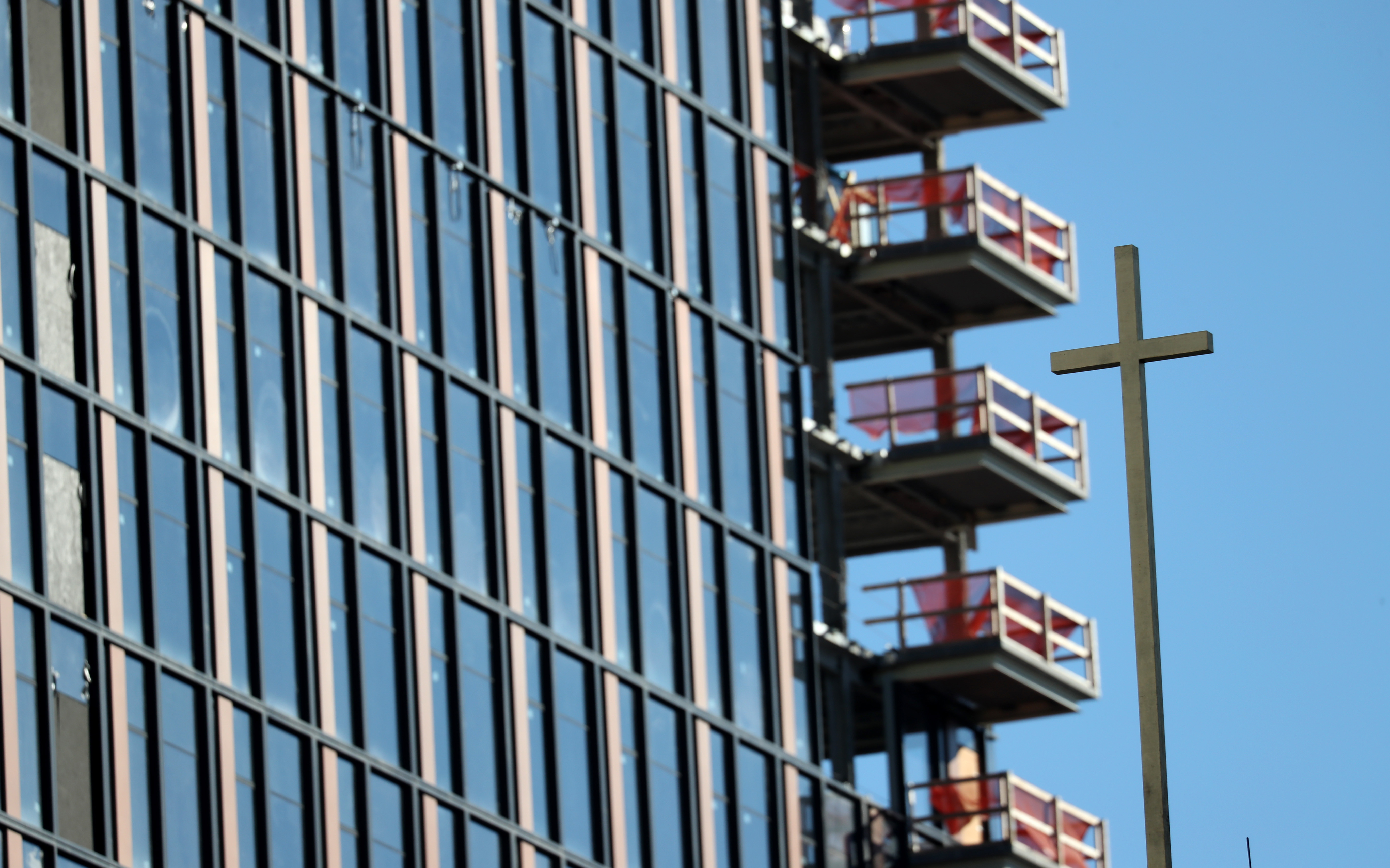 The cross atop the brick steeple on Our Lady of Good Voyage against the backdrop of new construction