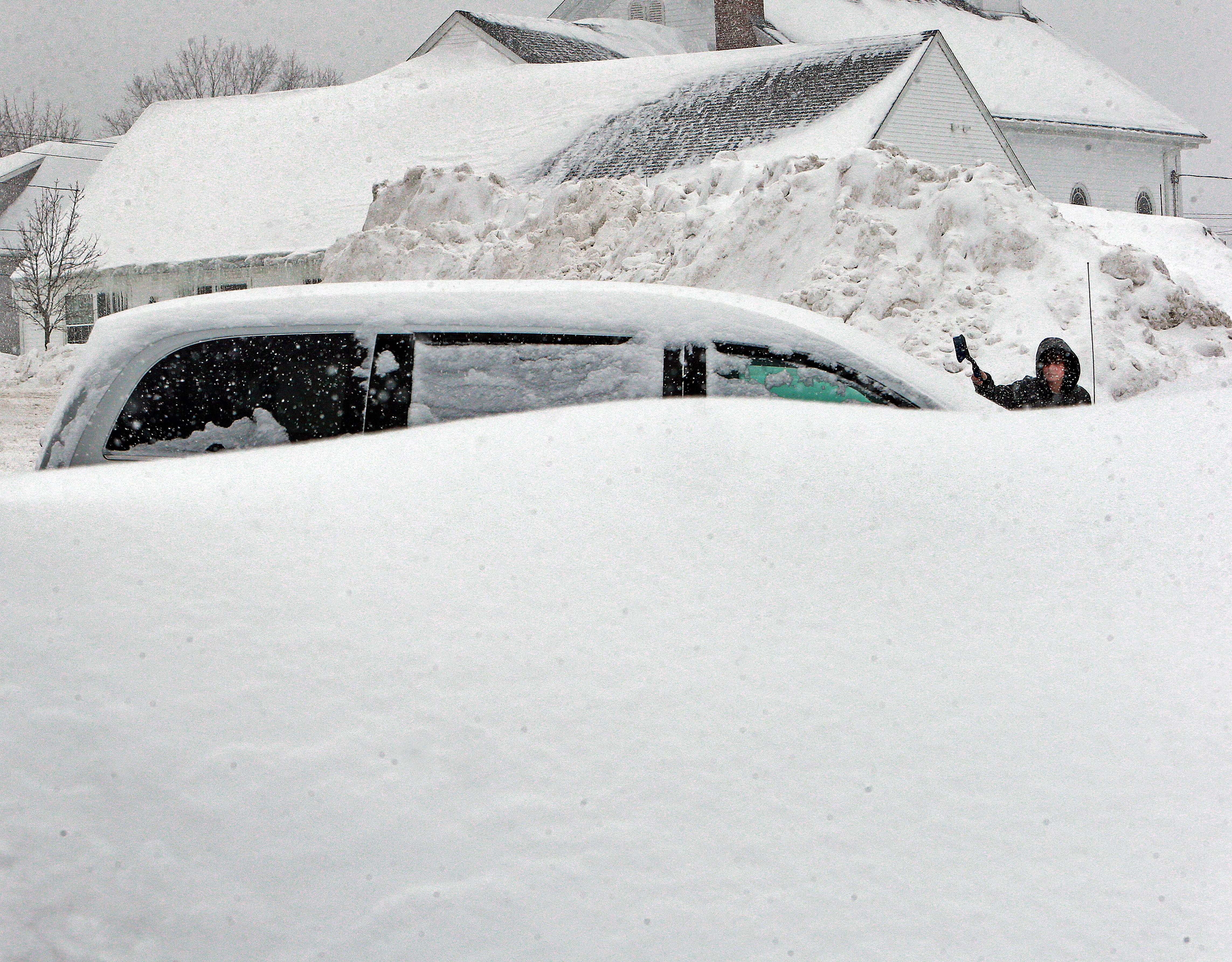 Ryan Burke of Lynn cleared a car of snow in a parking lot behind St. Michael Church in North Andover on Monday. The pile behind him was amassed during earlier storms.