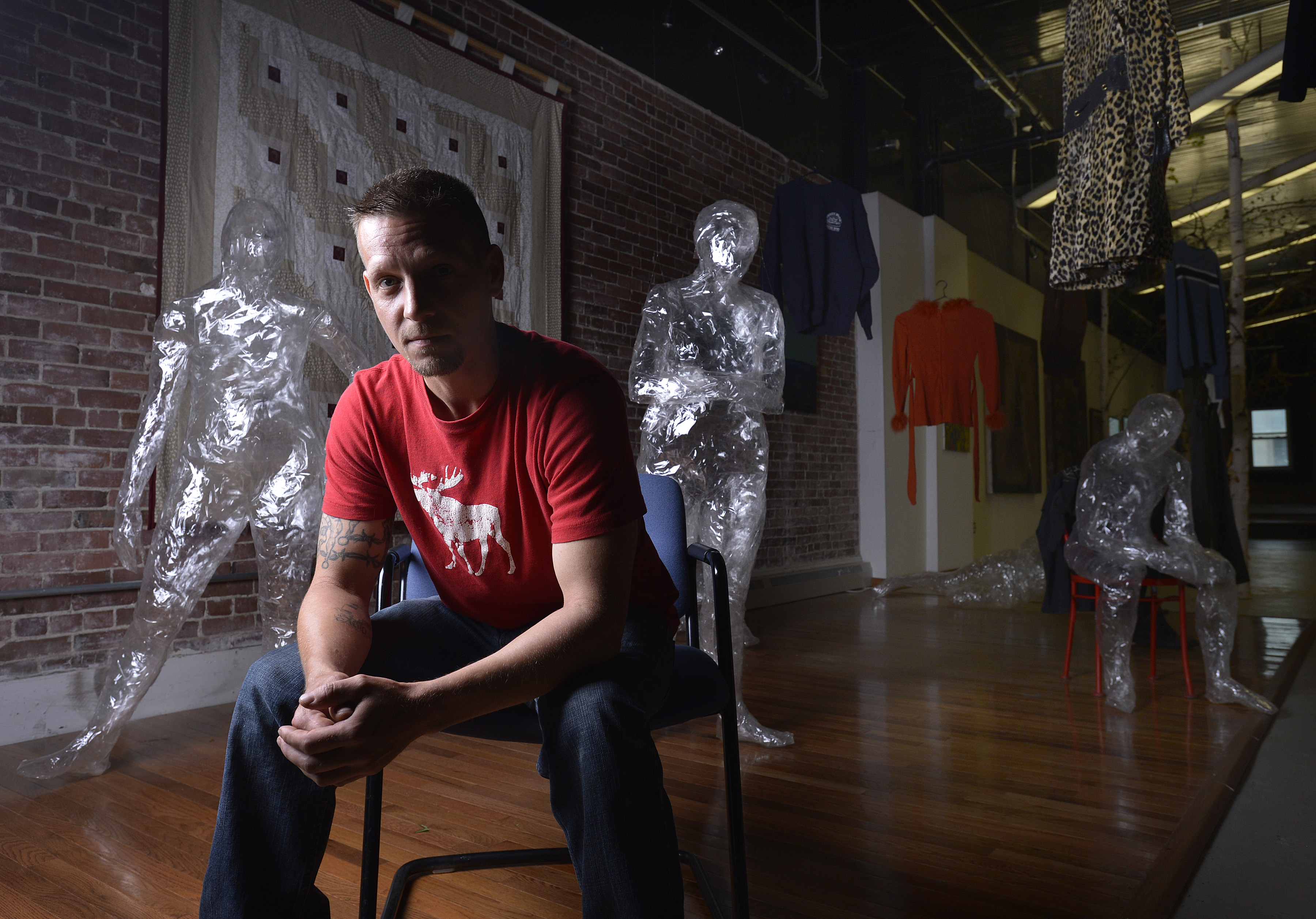 Shawn Dobson, a recovering addict who has received help from Grace Street Services, is pictured surrounded by an art piece called “Poppy Fields of Maine,” which displays human figures made of adhesive tape and clothing from drug overdose victims who have died.