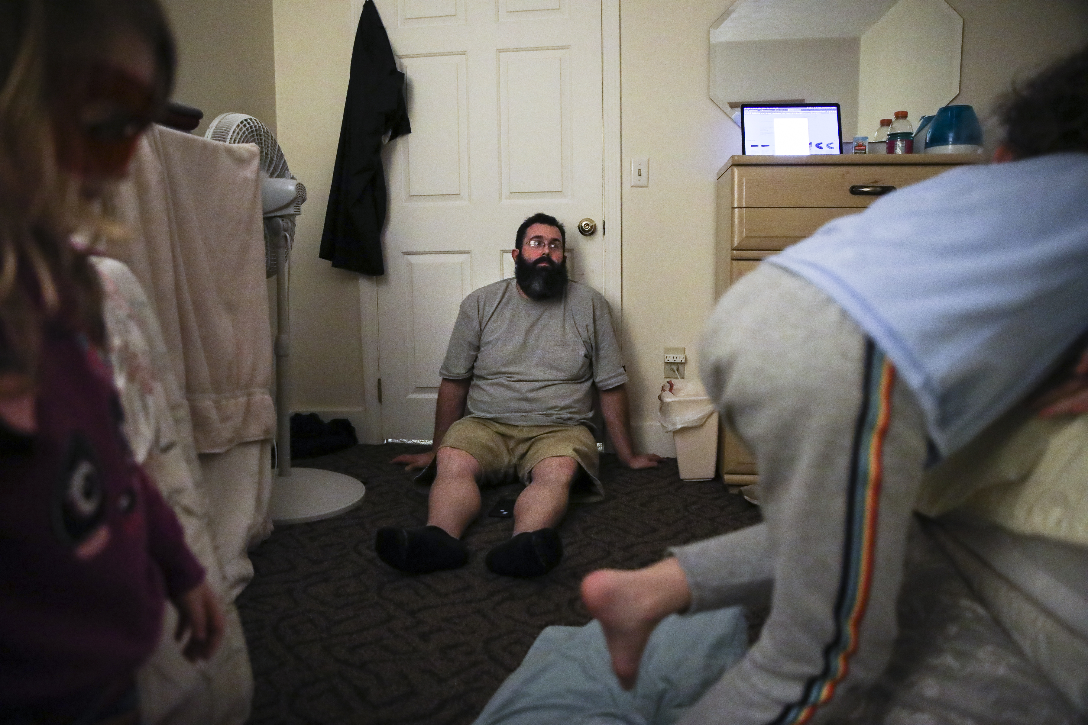 Exhausted, Patrick leaned against the bedroom door at the shelter while Laya (left) and Evan jumped back and forth on the bed. Often sharing one large room, the family of five was in much need of their own space.