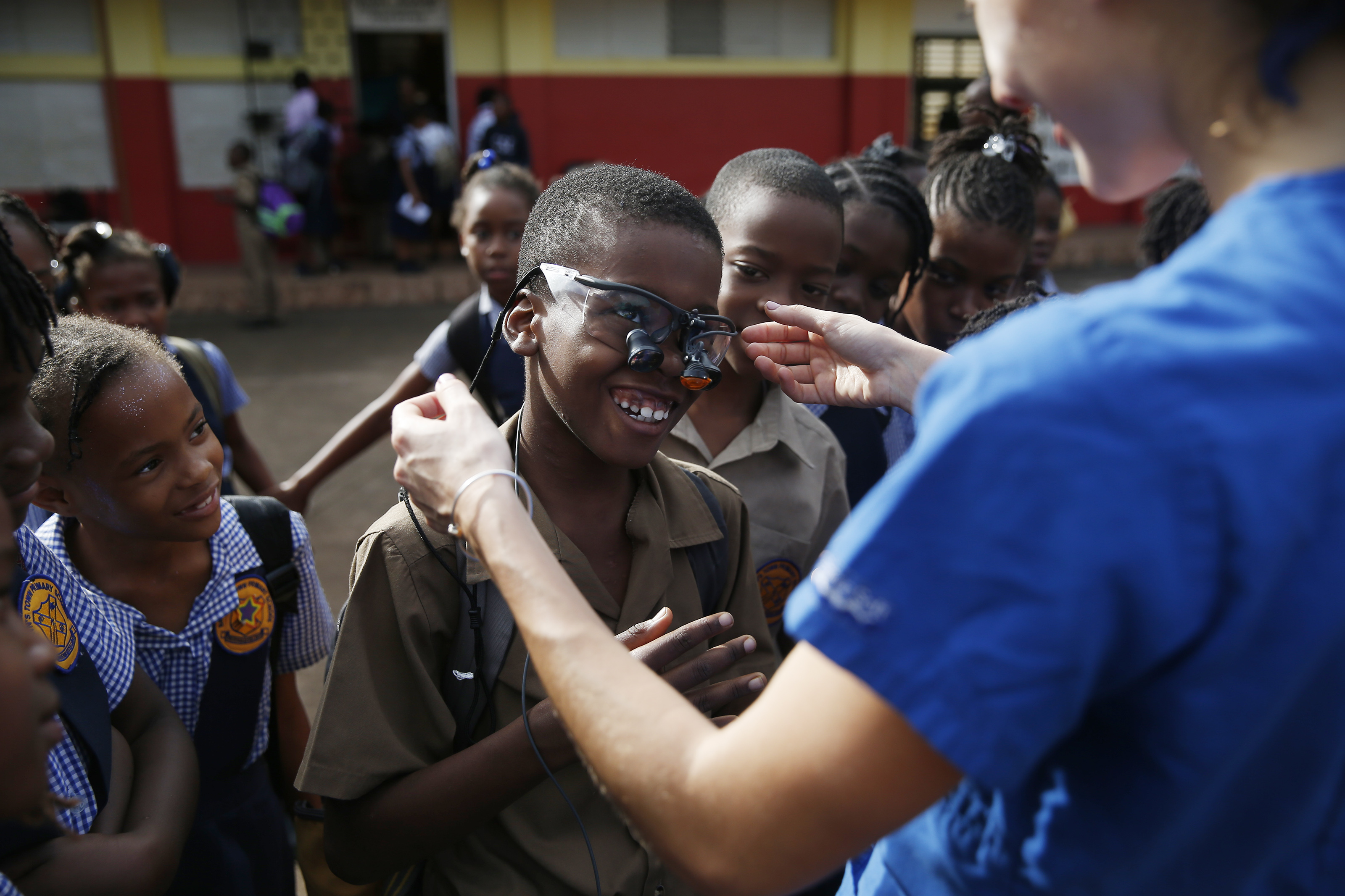 A boy at Brown’s Town Primary School laughed as Tufts Dental Student Toria Koutras fitted him with the glasses that she uses to examine teeth.