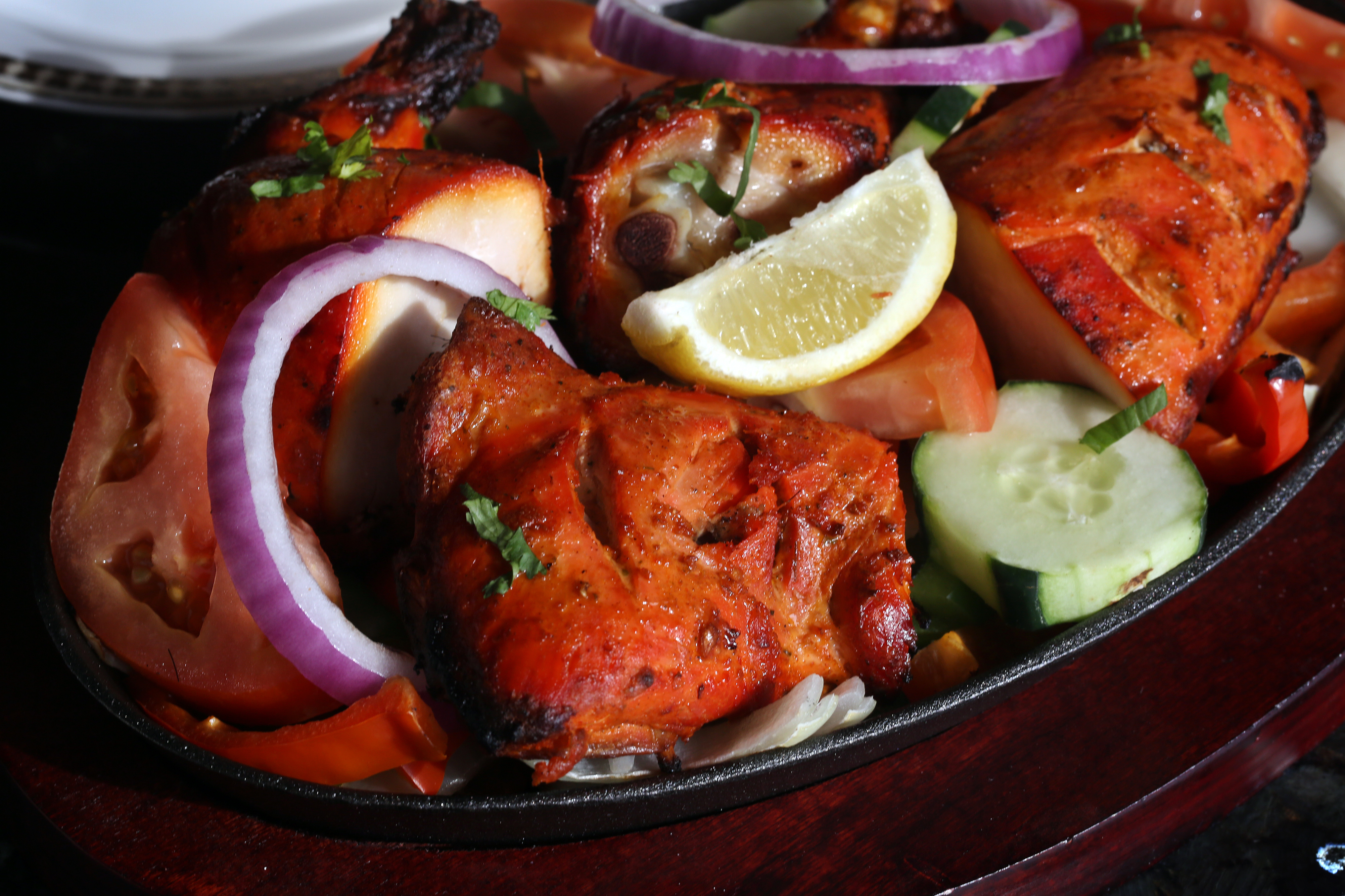 Tandoor chicken on a bed of onions, tomatoes, cucumbers, and carrots.