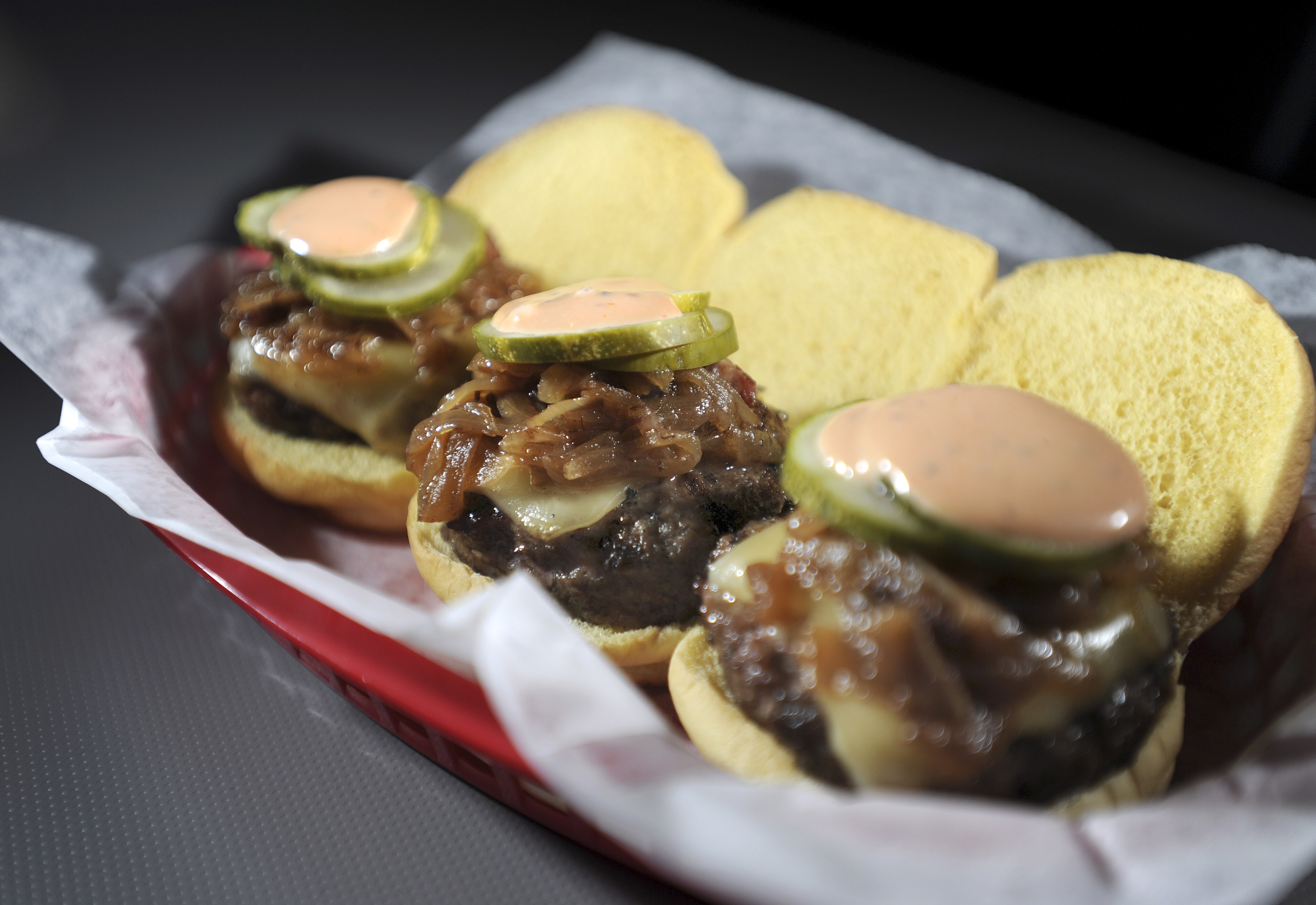 Three burgers topped with raclette, bacon-onion jam, pickles, and a tangy sauce.