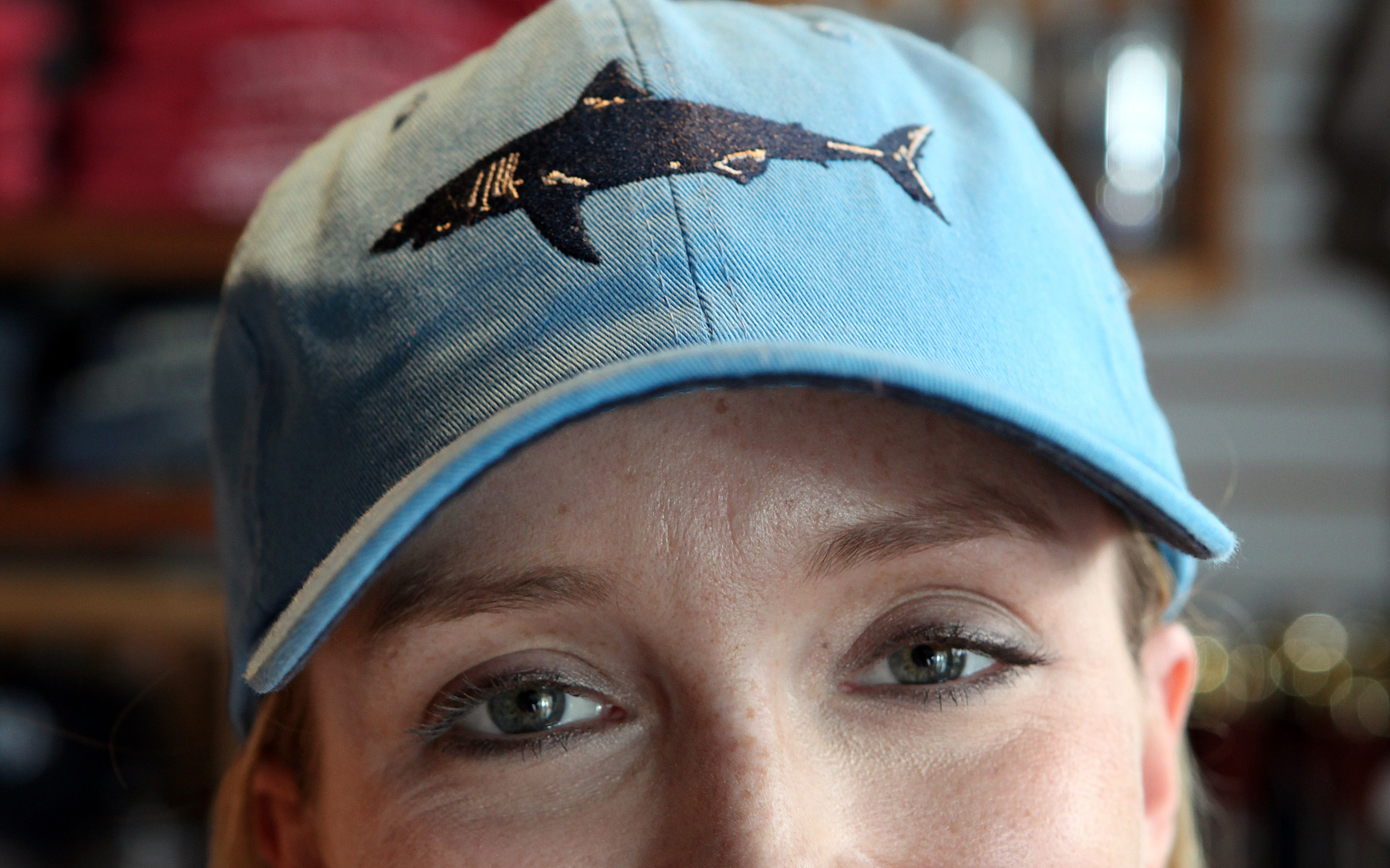 Sara Handler, inventory manager at Chatham Clothing Bar, models one of the store’s popular hats. Worldwide, shark tourism generates as much as $314 million a year, according to one recent study.