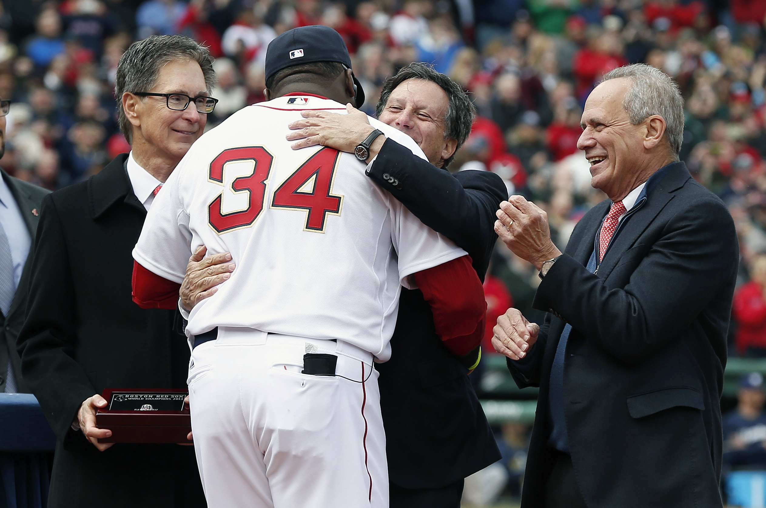 Red Sox slugger David Ortiz hugs Tom Werner, much to the approval of John Henry (left) and Larry Lucchino during pregame ceremonies before the home opener. Ortiz was presented with his World Series ring and additional ring for being named Series MVP.