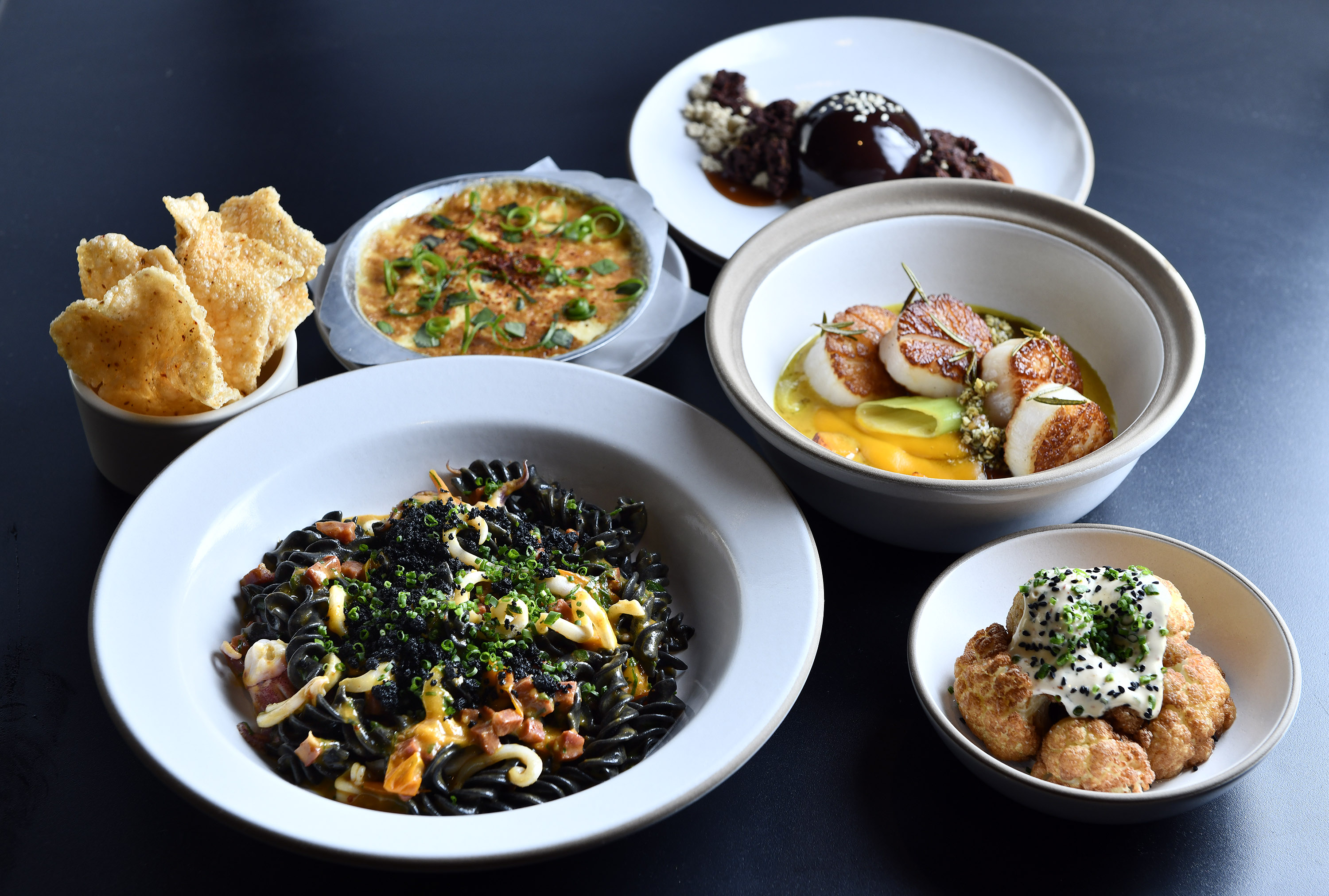 Clockwise from bottom left: squid ink fusilli, crab gratin with puffed rice crackers, chocolate semifreddo, scallops, and fried cauliflower at Chickadee.