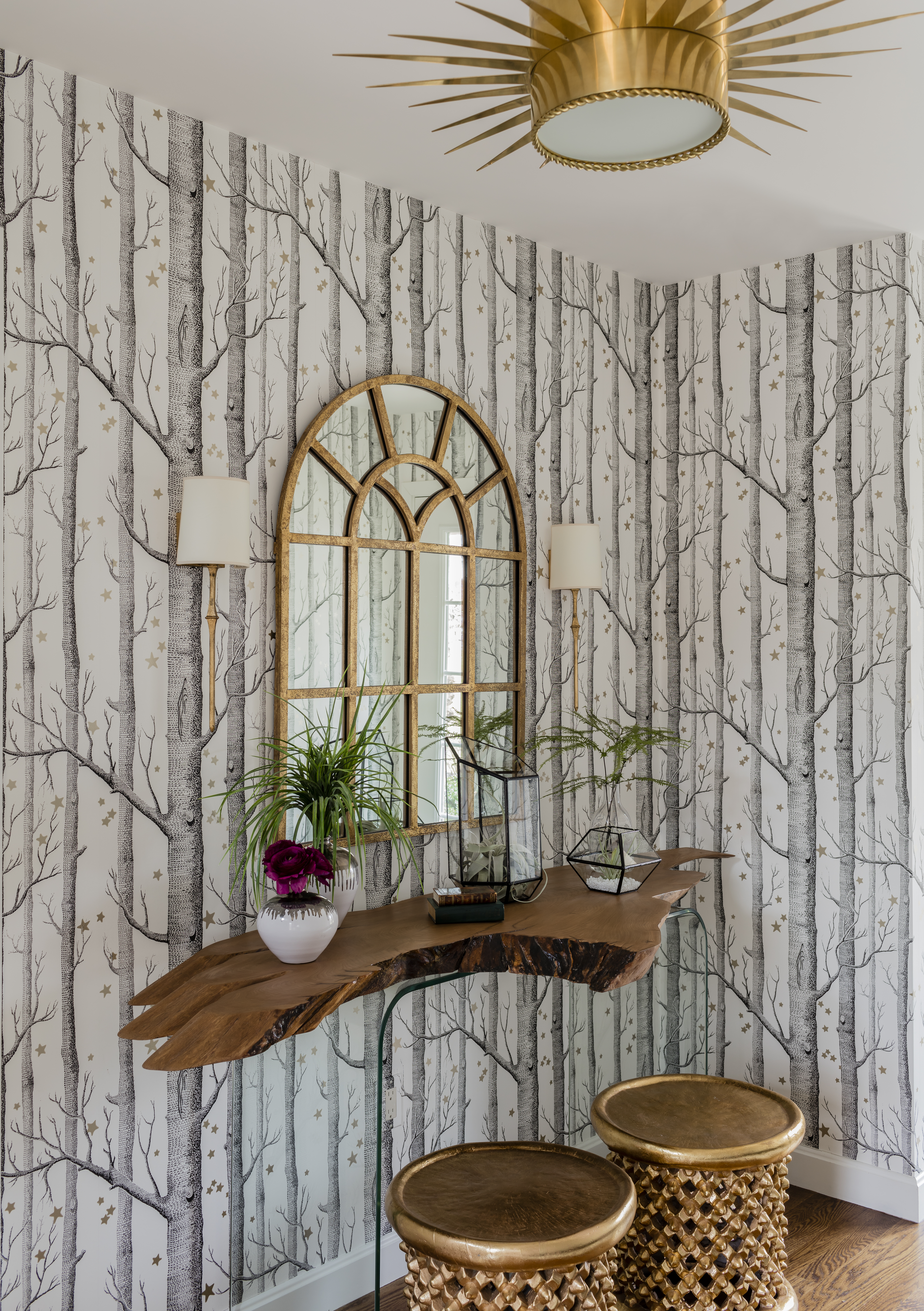 The elegant mudroom features a flush-mount light fixture that echoes the stars in the tree-motif Cole & Son wall covering. Gold stools are from Bungalow 5.