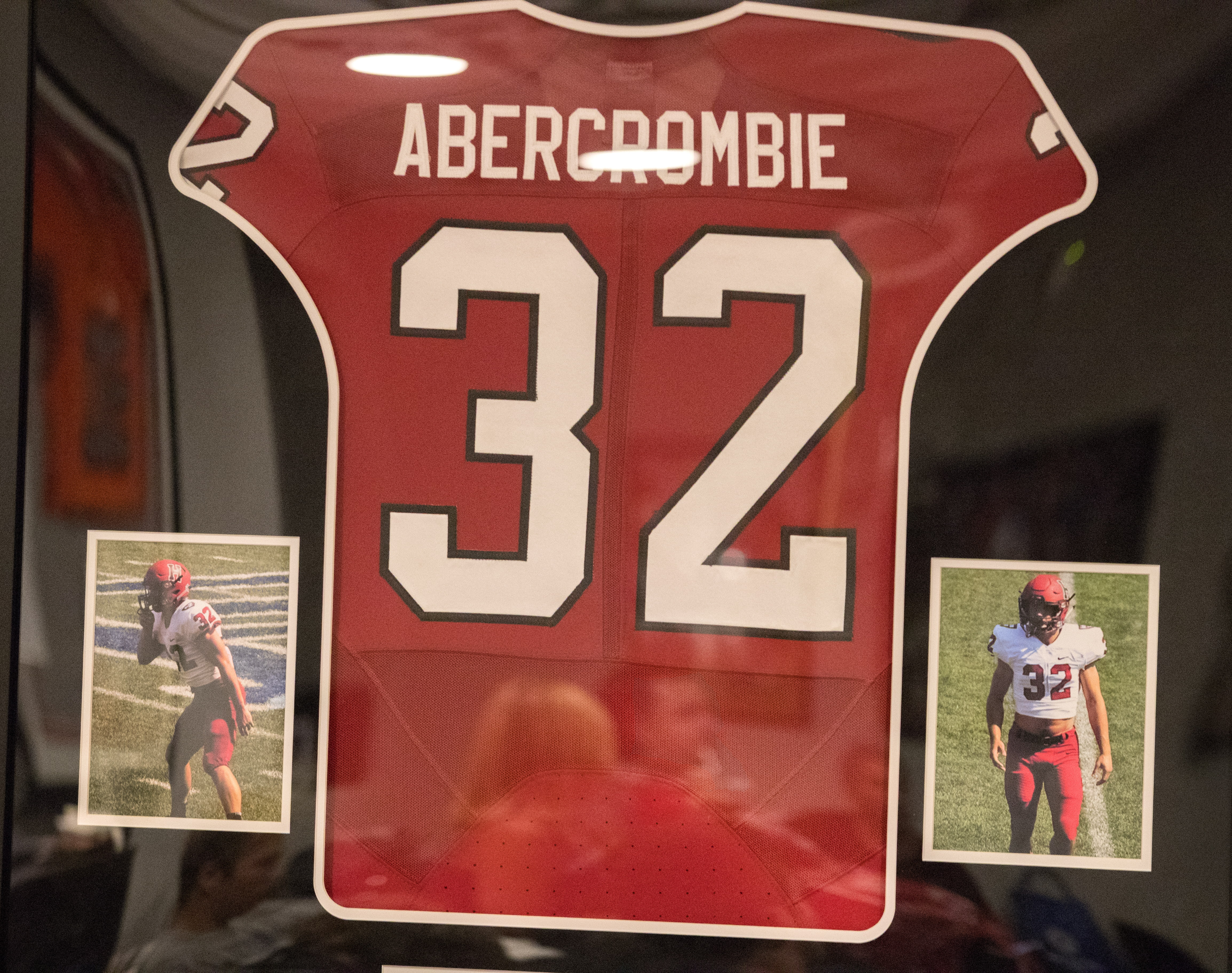 Ben Abercrombie is reflected in his Harvard Crimson jersey hanging on a wall.
