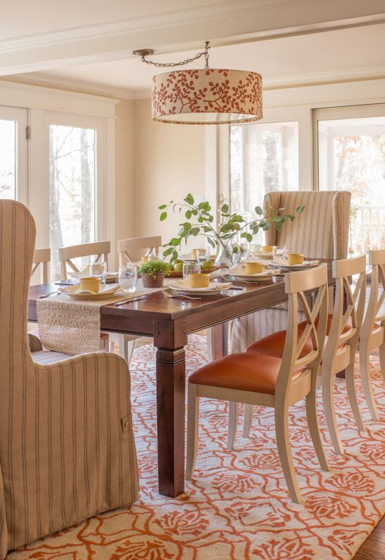 The dining table is lightened with an orange patterned rug and white side chairs with orange vinyl seats.