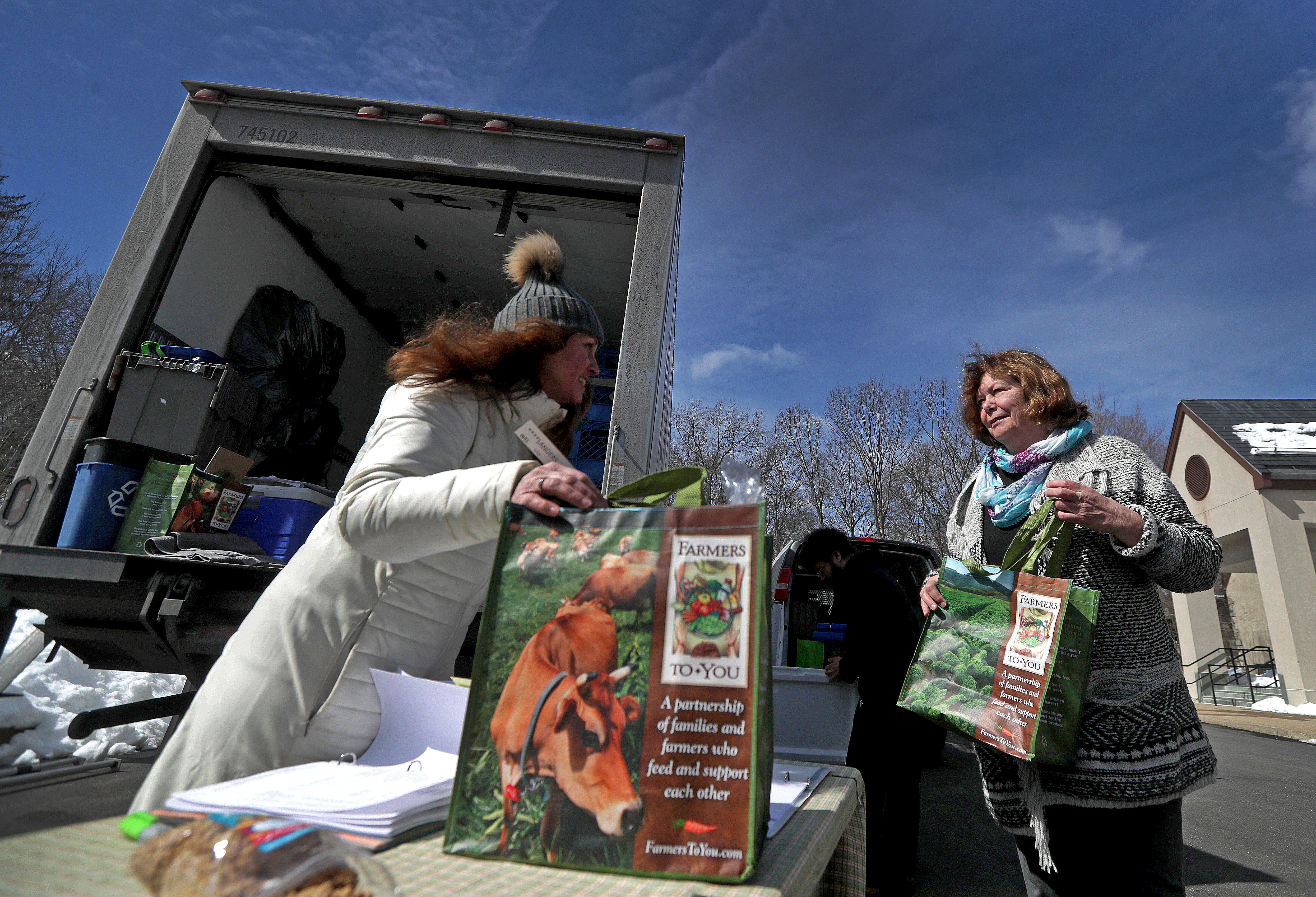 Site host Janine Malone (left) greeted Wellesley resident Laurel Landers, who came to the parking to pick up her food order.