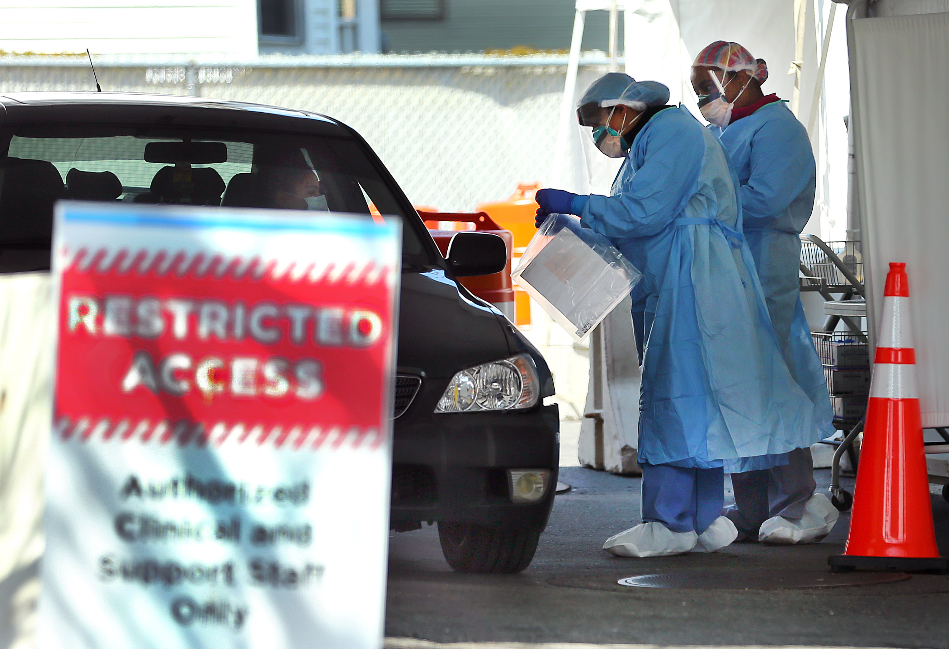 Health care workers perform a COVID-19 test on a patient in a drive-through testing site set up in the parking lot of the Bowdoin Street Health Center in Dorchester.
