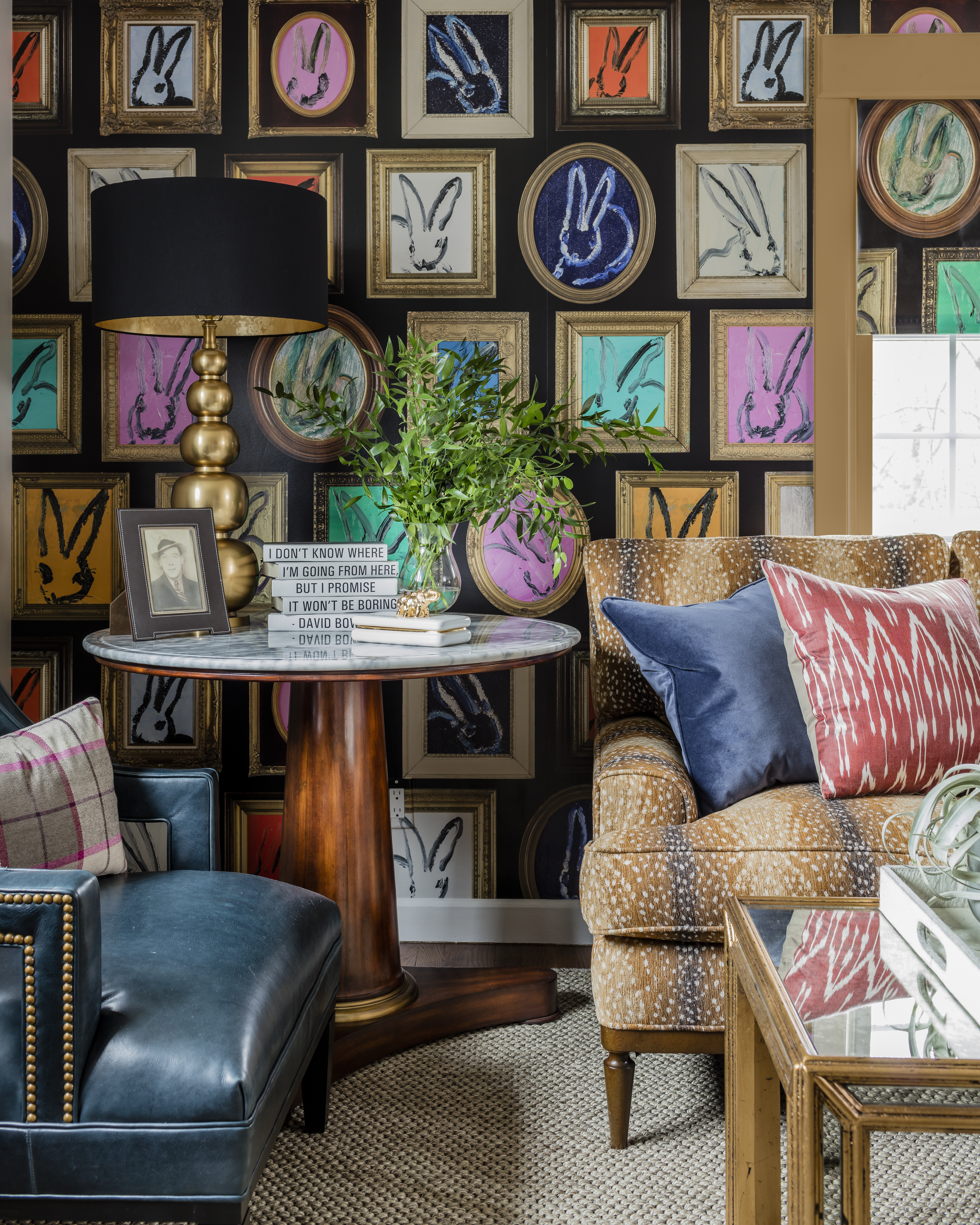 In the living room, the Hunt Slonem for Lee Jofa wallpaper takes center stage. The antelope-pattern chenille Wesley Hall sofa holds bold-hued throw pillows. A Wesley Hall blue leather armchair adds a textural dimension. The marble-top table is by Lillian August for Hickory White.