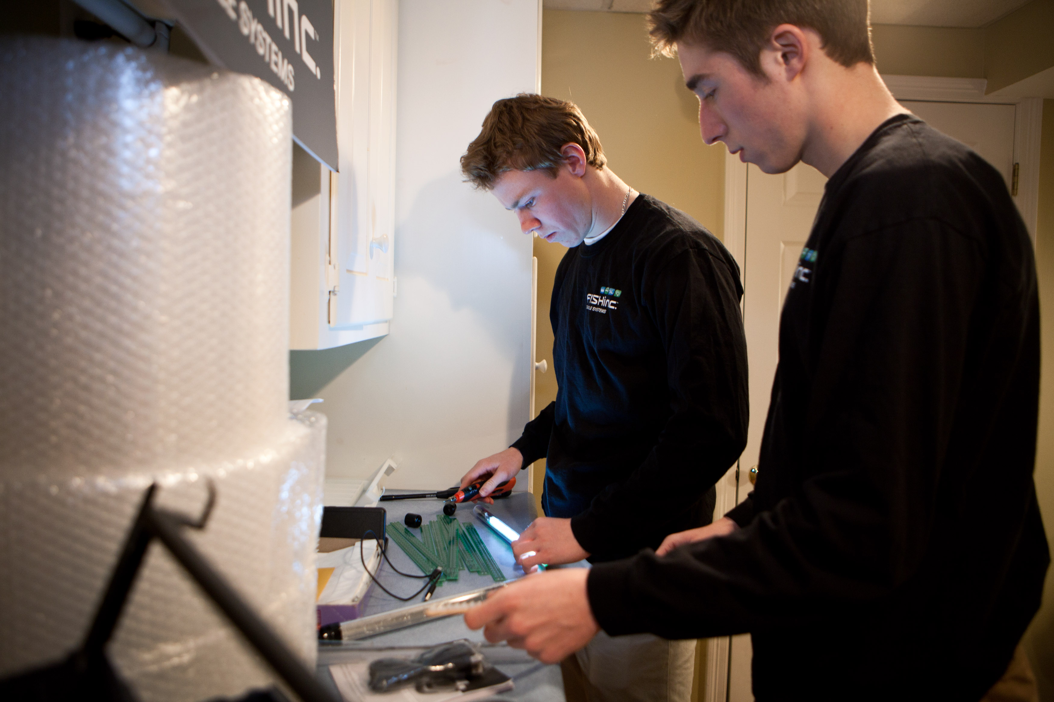 Adam Gibbs (left) and Nick Bongi soldered together pieces for the ProGlo+ in their basement work space in Westbourough. The two 18- year-olds have started a Kickstarter campaign to fund their invention, so far raising nearly half of the $30,000 they are seeking.