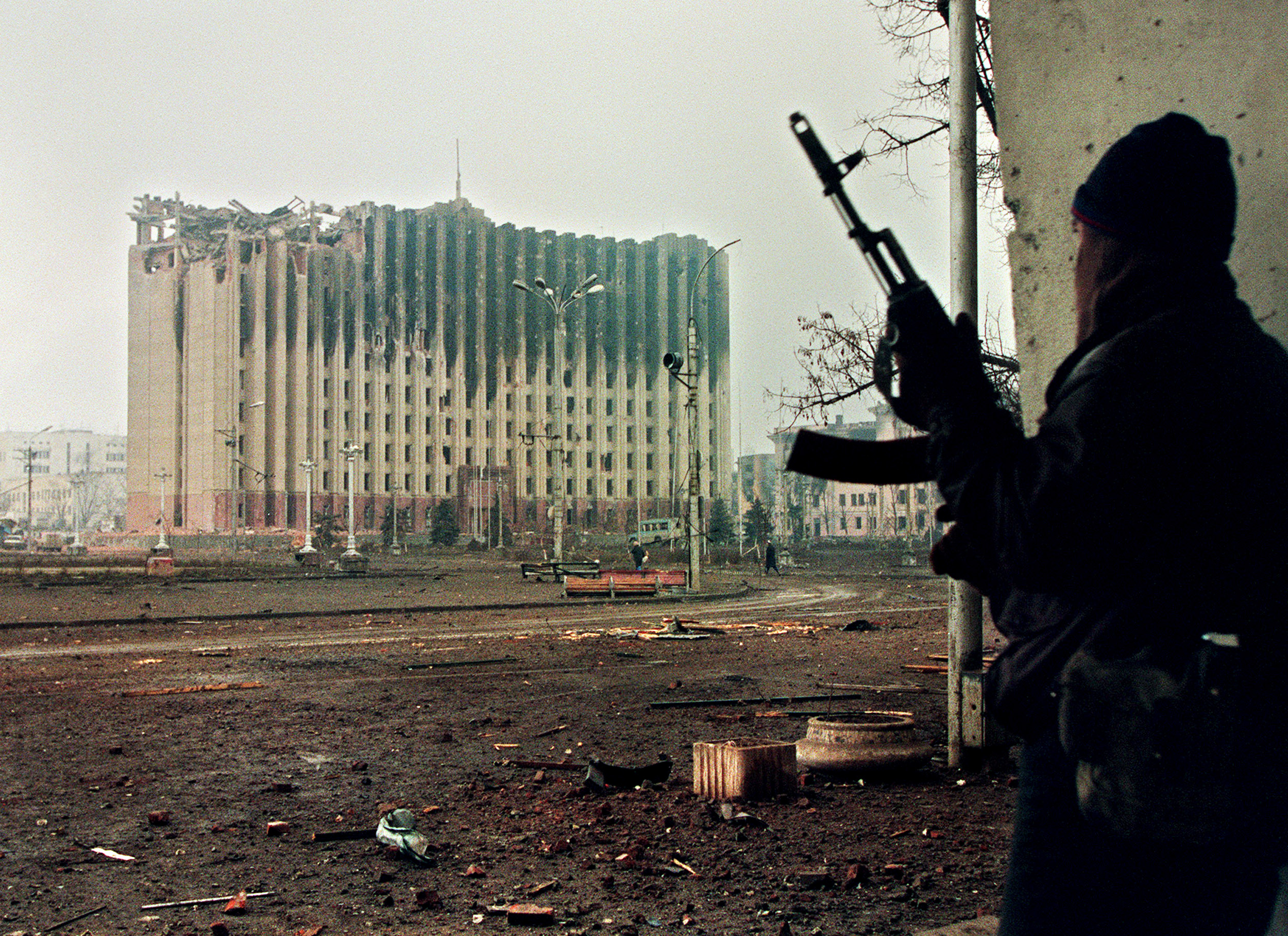 A Chechen fighter took cover from sniper fire in Grozny in 1995. Across the square, the presidential palace sat in ruins after Russian artillery bombardments.