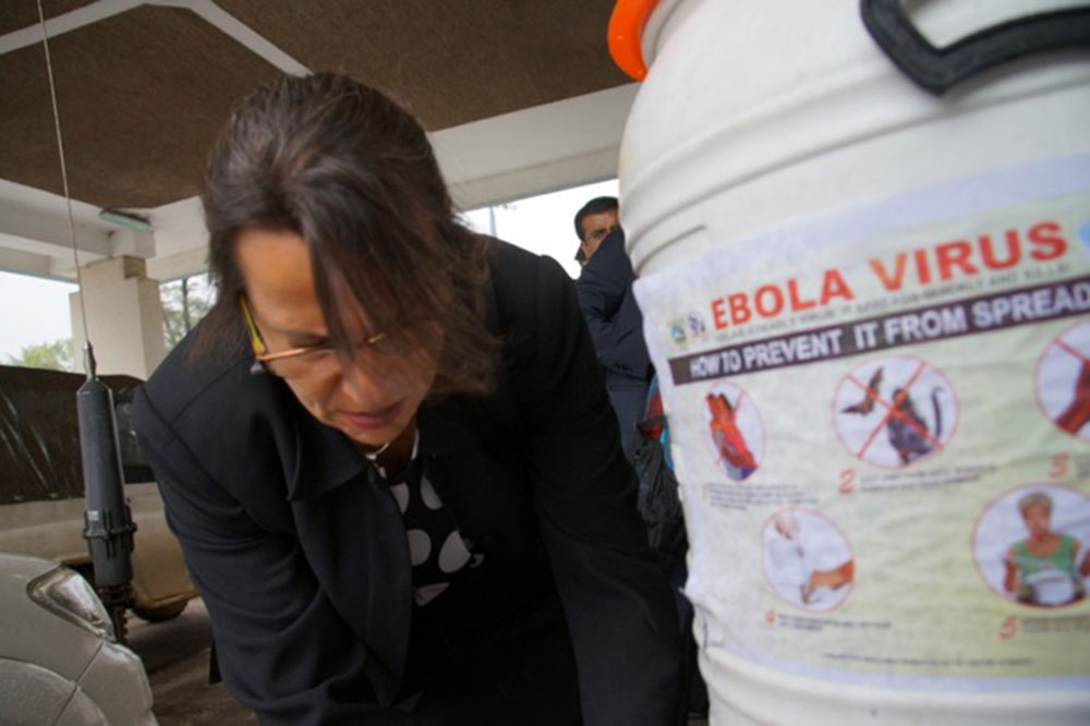 Dr. Joia Mukherjee of Partners in Health washed her hands with water and bleach solution before entering a public building in Monrovia.