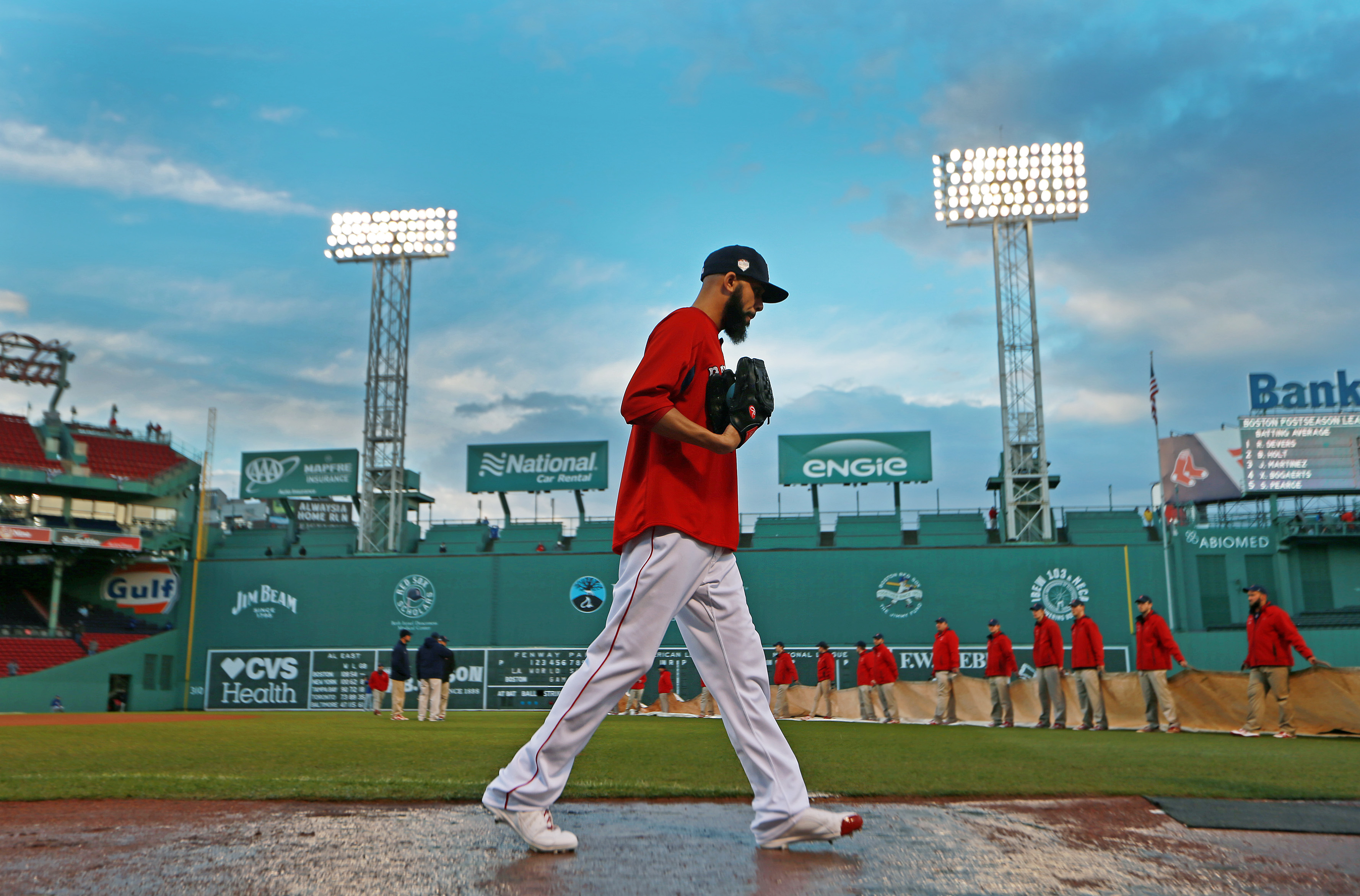 After a rain storm moved through the area, David Price walked on the wet dirt, while in the backround, the grounds crew, who had removed the tarp to clear it of standing water, were ready to put it back on over the infield.