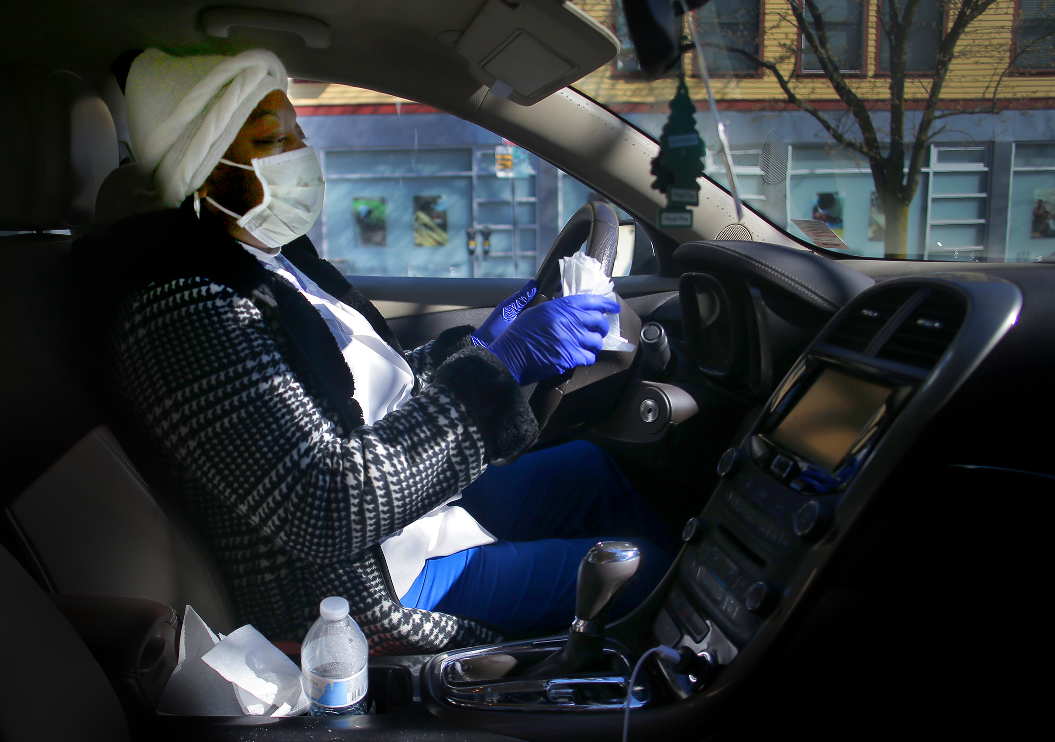 Personal care assistant Maria Colville leaves her home in Cambridge to care for an elderly woman in Watertown. She leaves her building in a mask and wearing rubber gloves, and wipes down the interior surfaces of her car with disinfectant before taking the gloves off.
