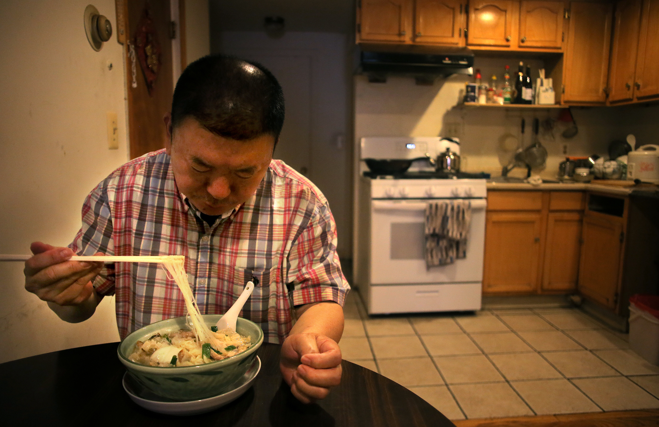 Gaoxin Wu enjoyed his lunch of noodle soup in the kitchen of his Beach Street apartment.