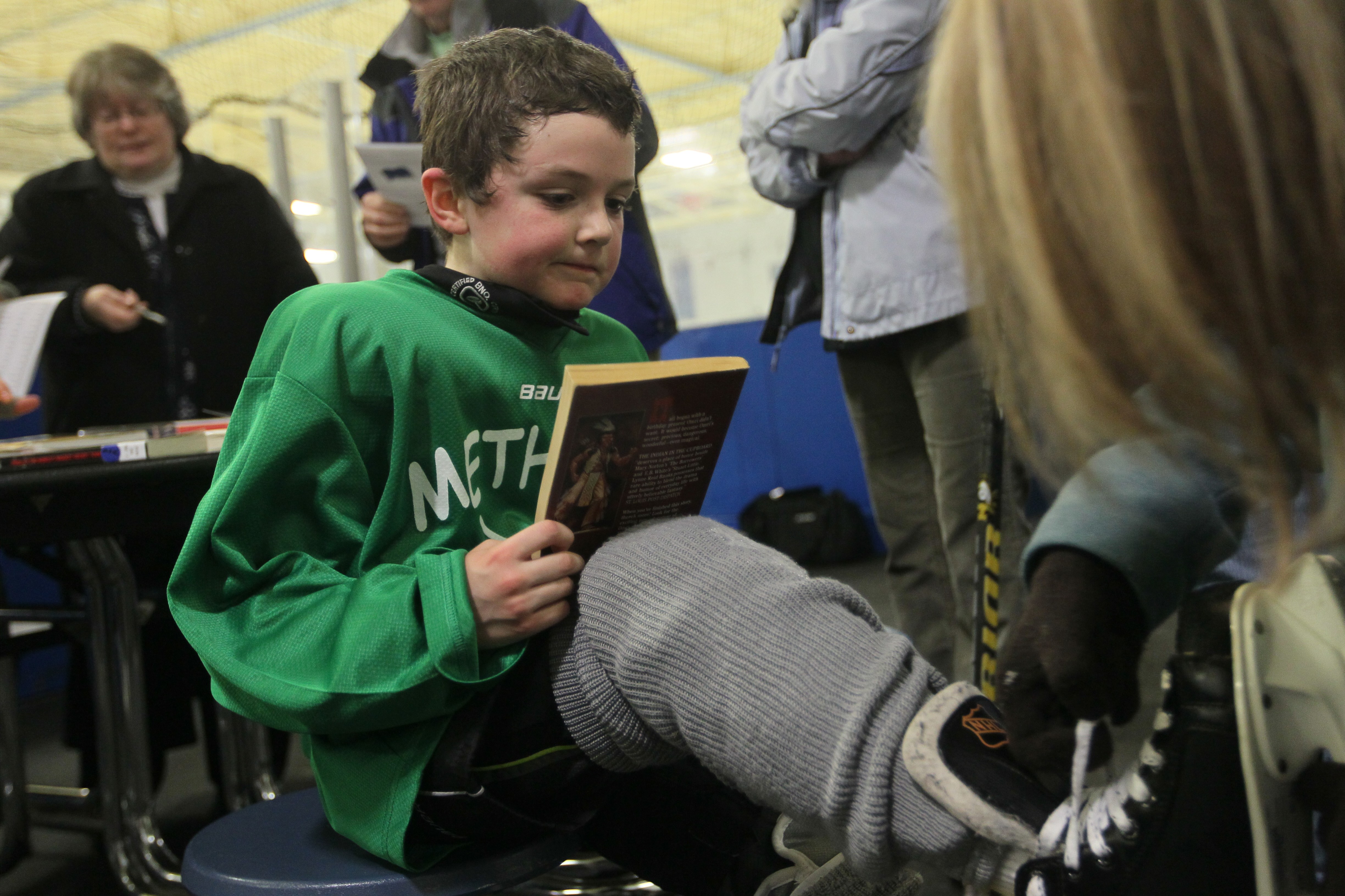 Owen Howell, 8, holds a book he just checked out as part of Methuen Fun Hockey League’s Skate & Read program, while mom Christine pulls off his skates after practice.