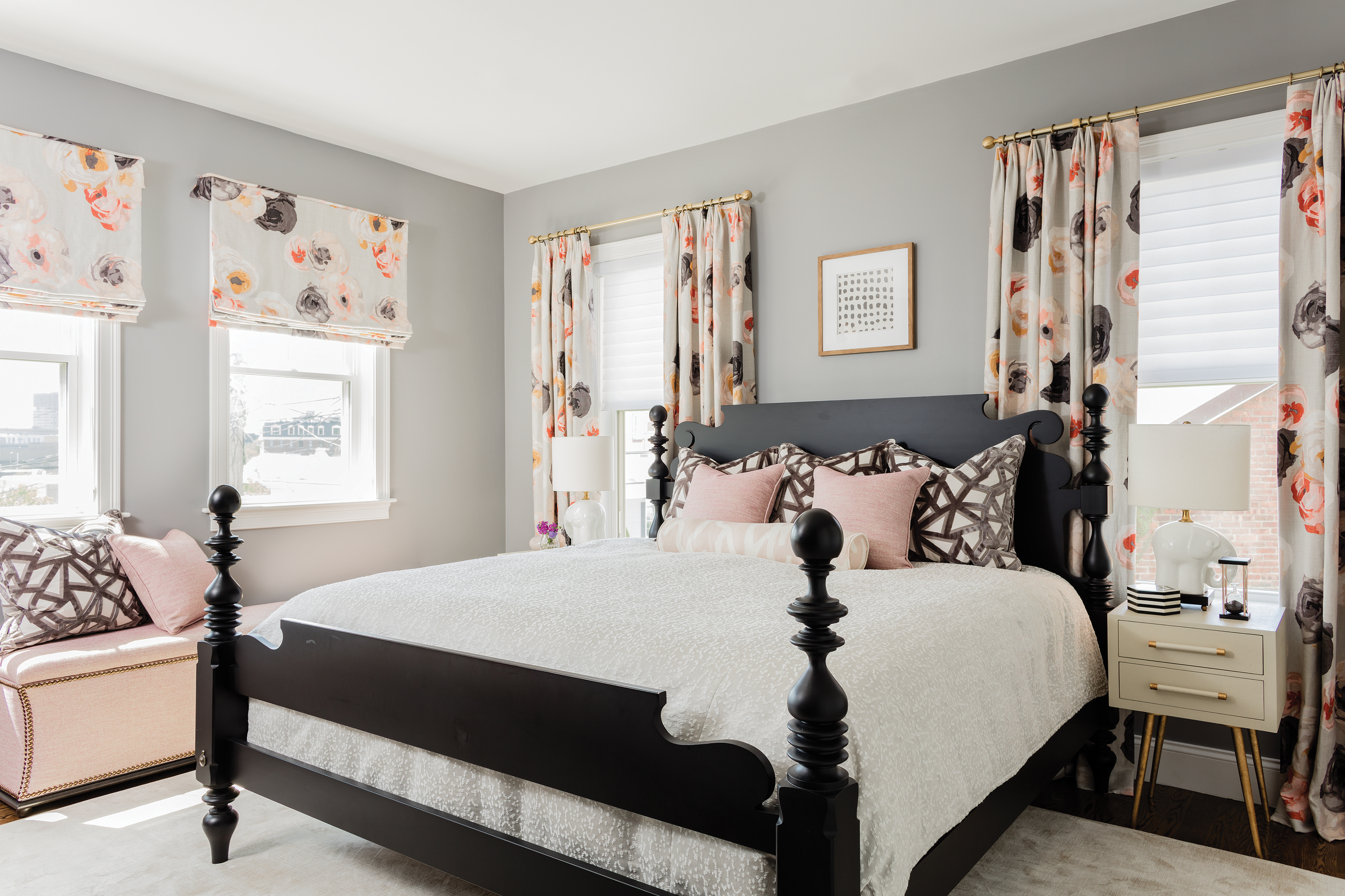 In the master bedroom, the drapes feature a pink floral motif to liven up the space’s mostly gray and black scheme. The black four-poster bed pairs well with the neutral-toned Made Goods night stands, which have gold legs that add a little glam to the room. The storage ottoman was custom made by Kravet; the rug is by Stark.