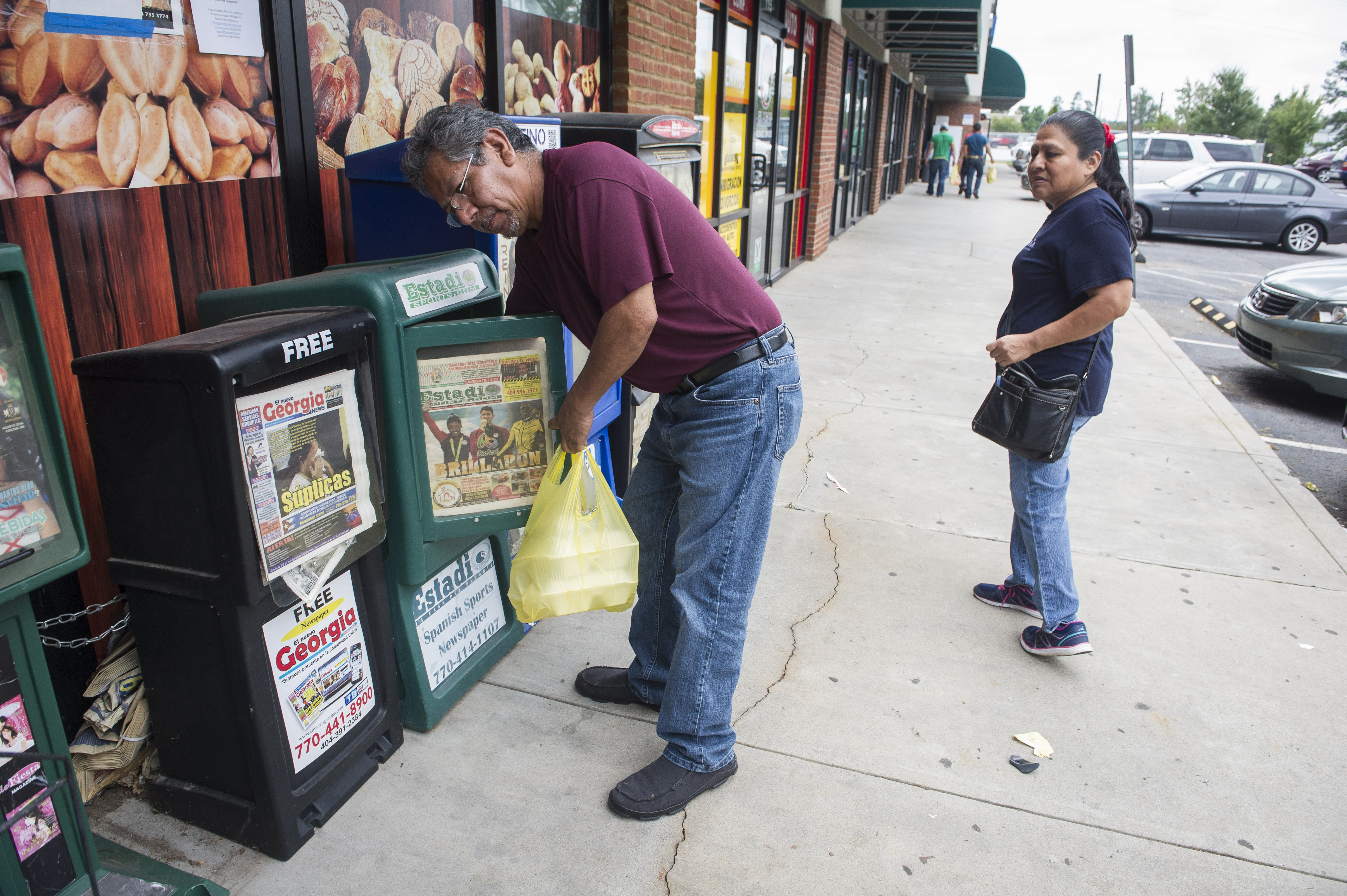Roberto Gonzalez, of Mexico, gets a newspaper out of boxes catering to the Hispanic community as his wife Cecilia, watched late last month in Norcross, Ga.