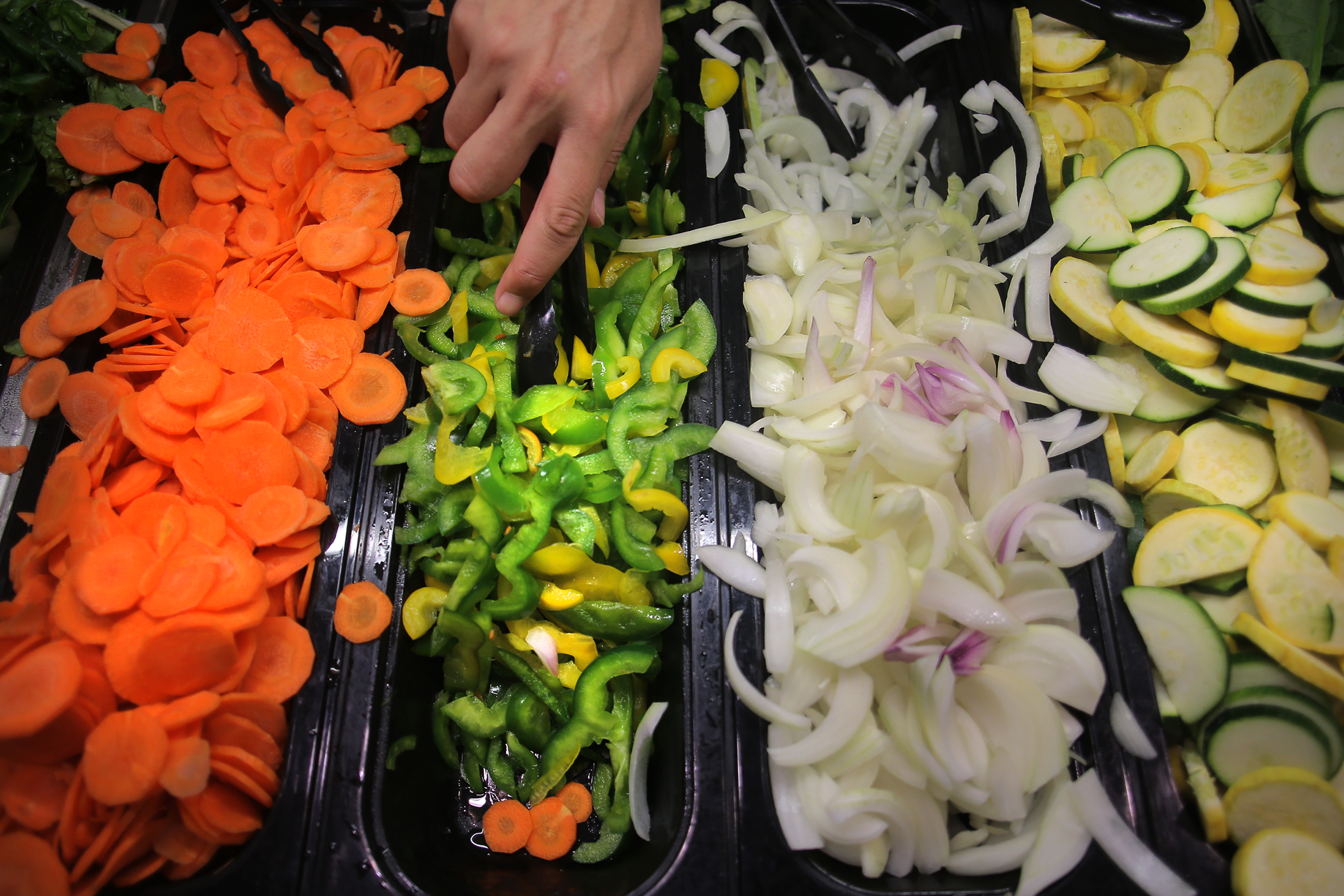 A student selected vegetables at a stir fry station.
