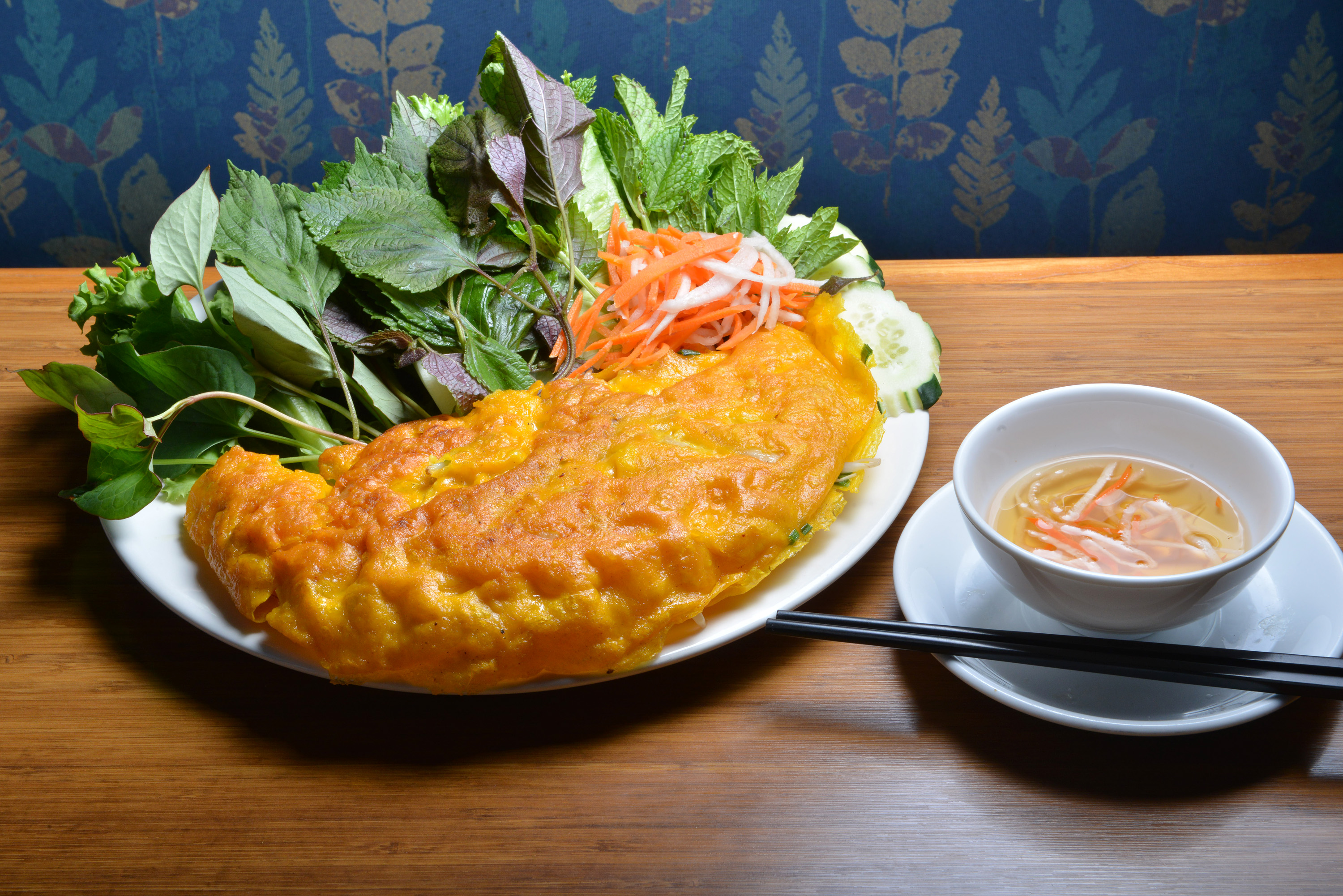 Banh xeo, rice flour rounds stuffed with shredded pork, shrimp, and bean sprouts, with vegetables and nuoc cham sauce.