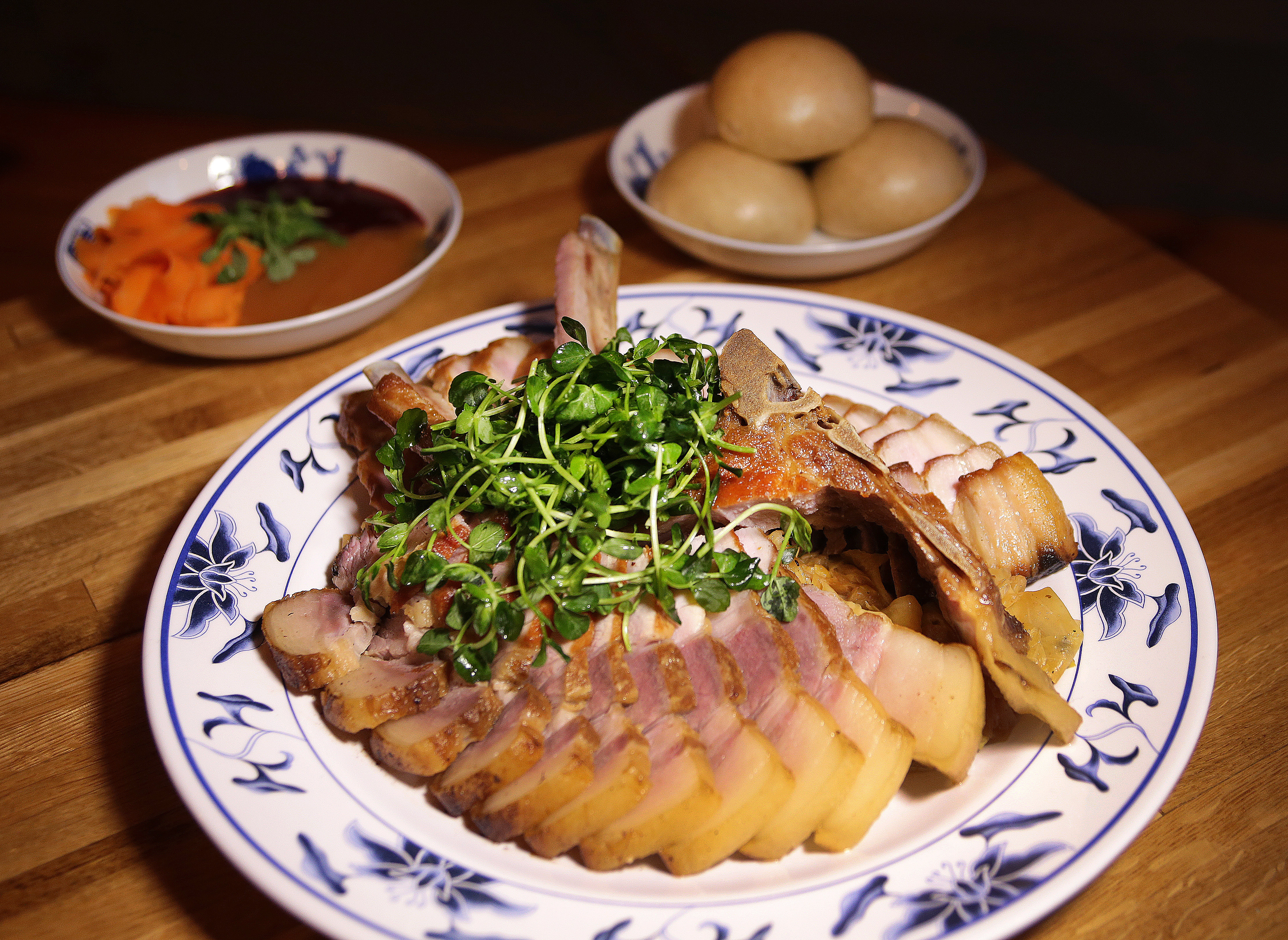A pork rib and belly chop with cabbage made creamy with miso, steamed buns, cranberry-hoisin sauce, apple jelly, pickled carrots, and pea shoots.